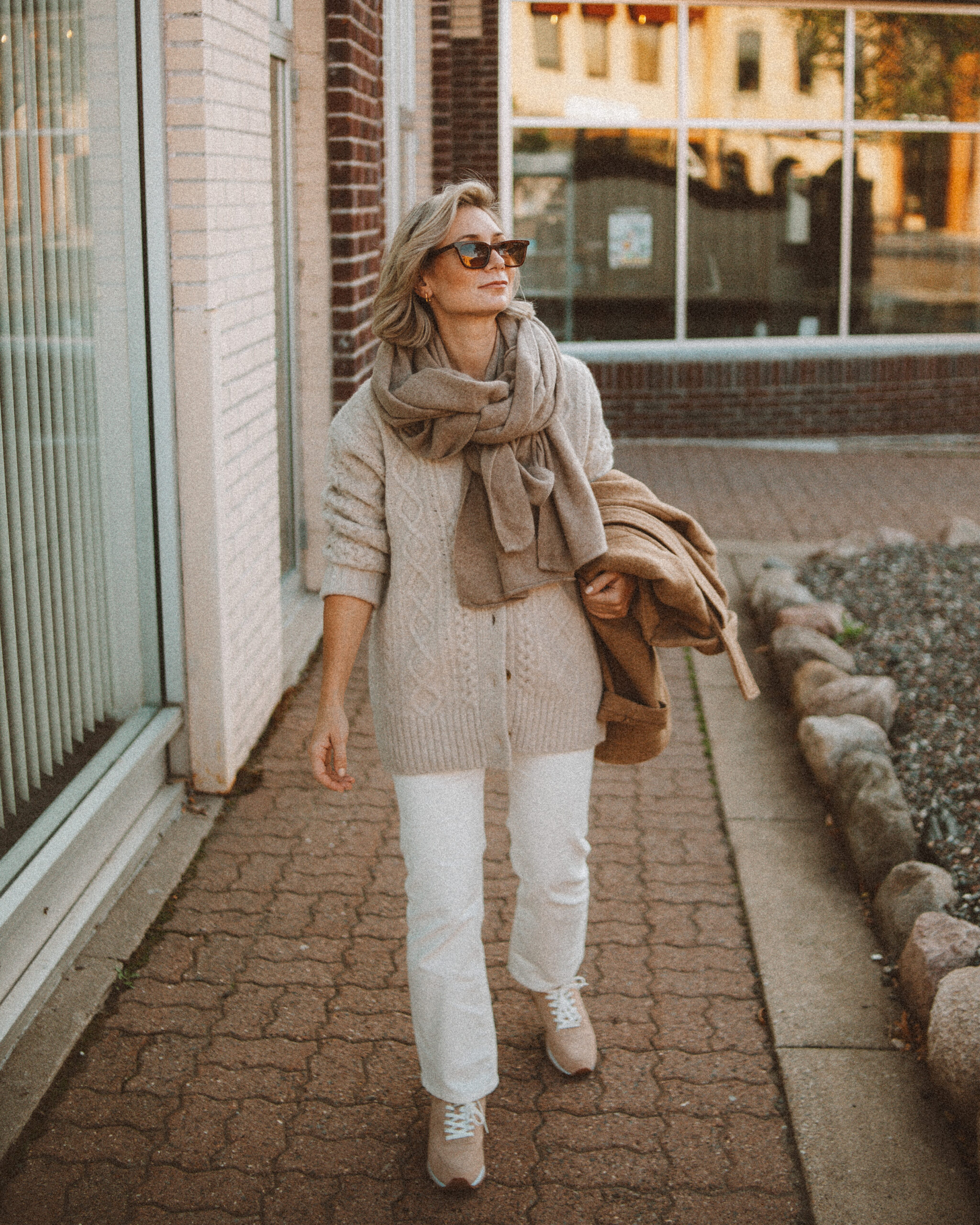 Karin Emily wears the perfect pair of corduroy pants with a cable knit cardigan, tan sneakers, cashmere scarf, and camel wool blazer coat