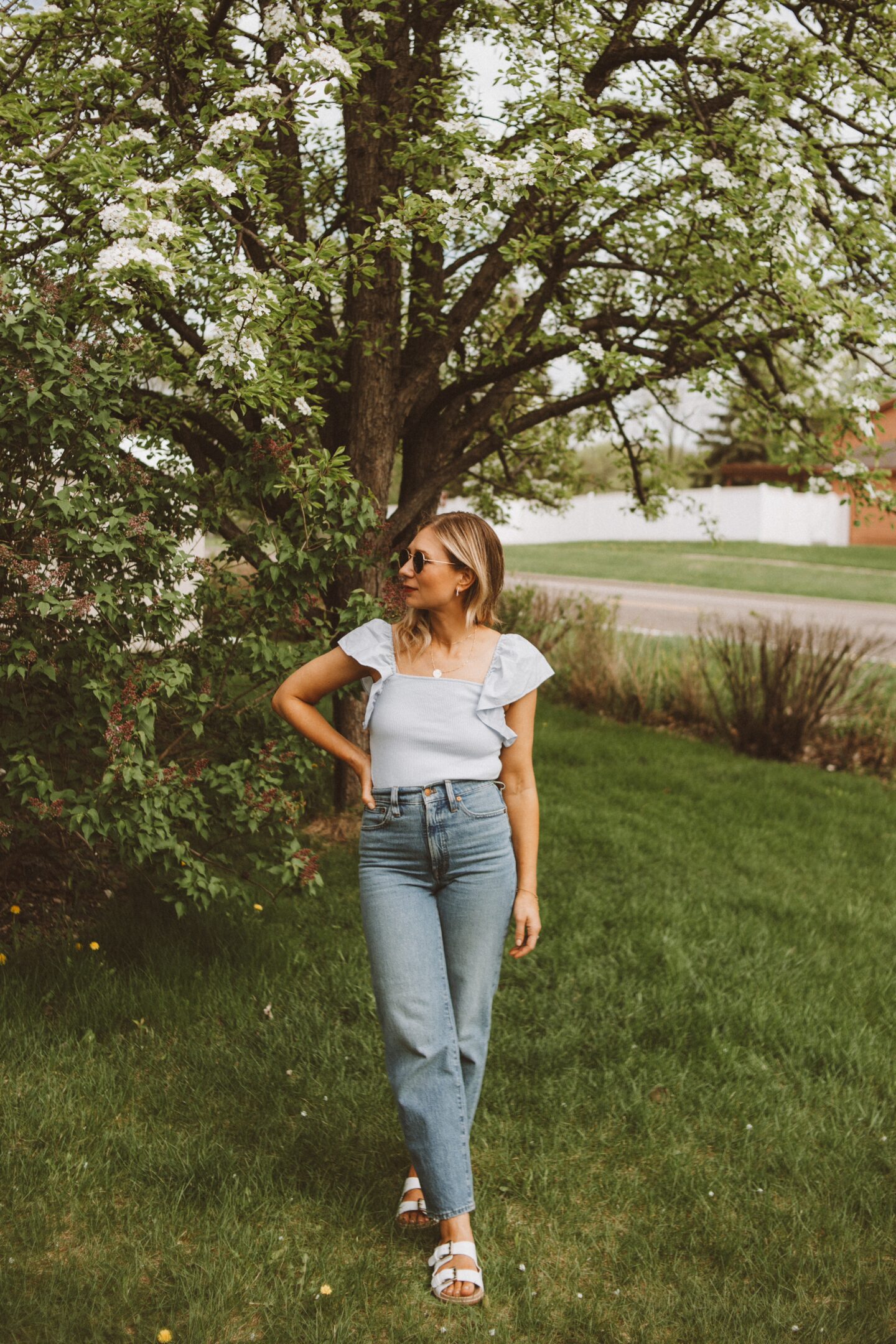 Karin Emily wears a blue flutter sleeve tank, straight leg cropped jeans, and sandals