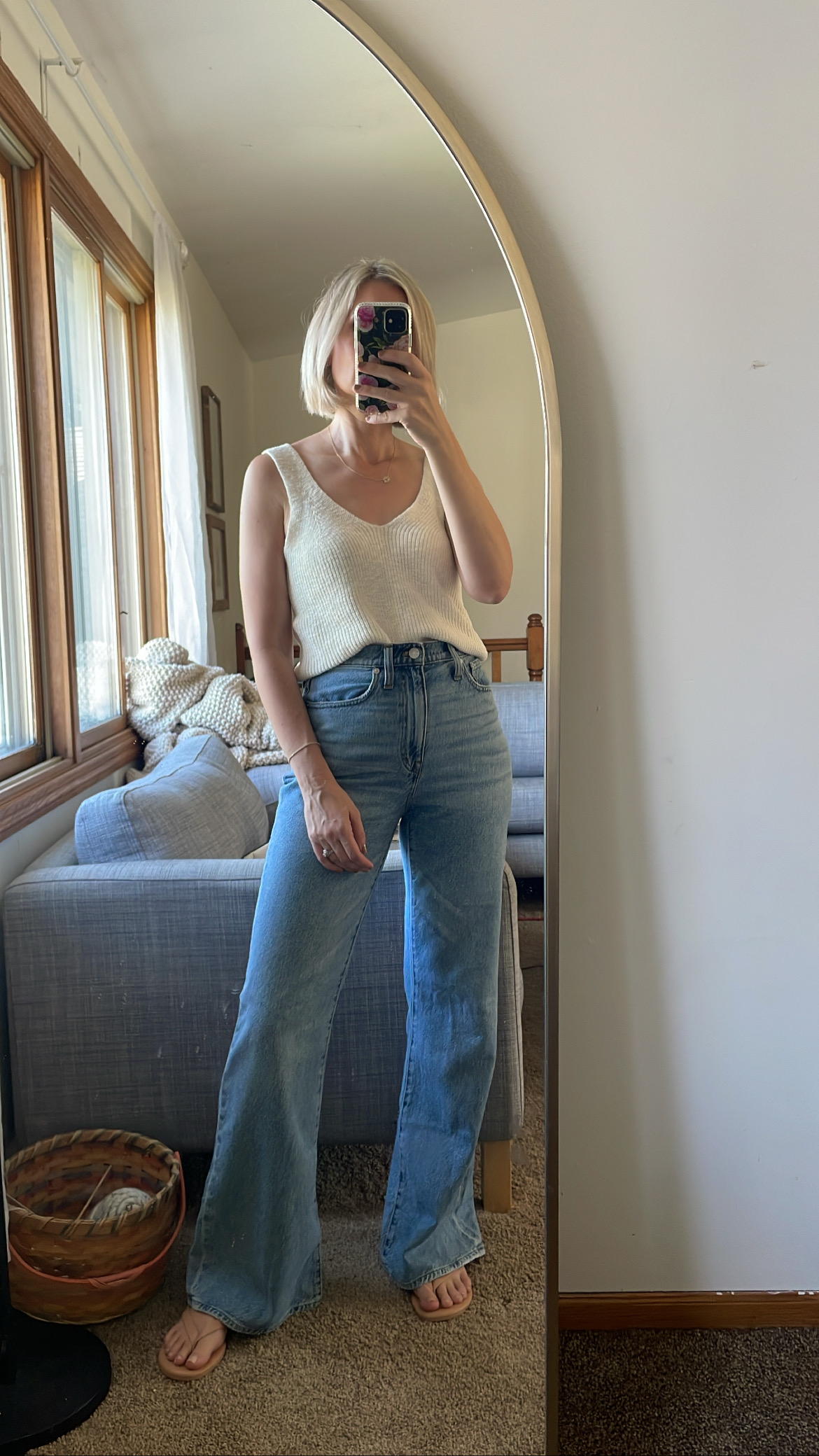 Karin Emily wears a white sweater tank, wide leg loose jeans, and flip flops