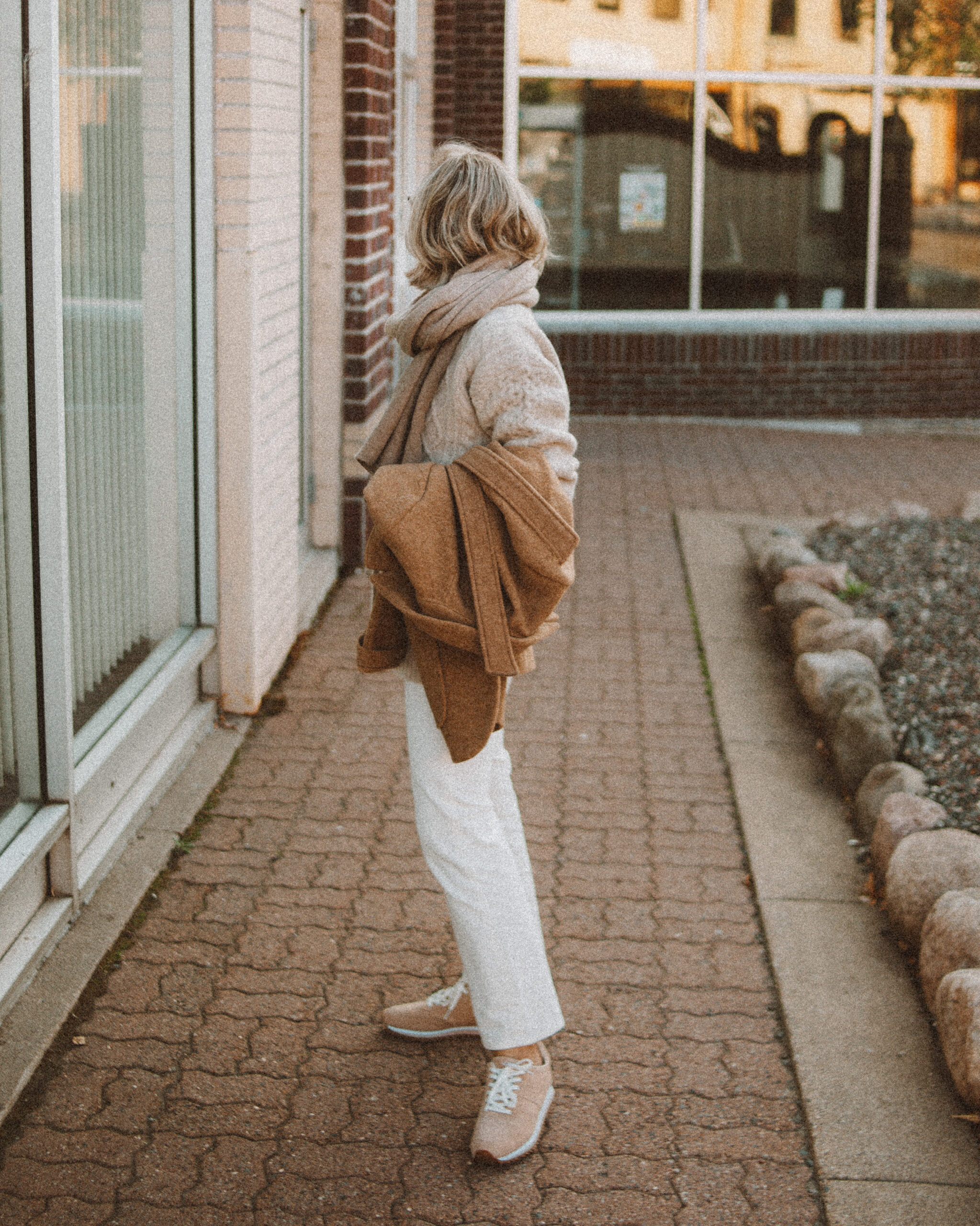 Karin Emily wears the perfect pair of corduroy pants with a cable knit cardigan, tan sneakers, cashmere scarf, and camel wool blazer coat