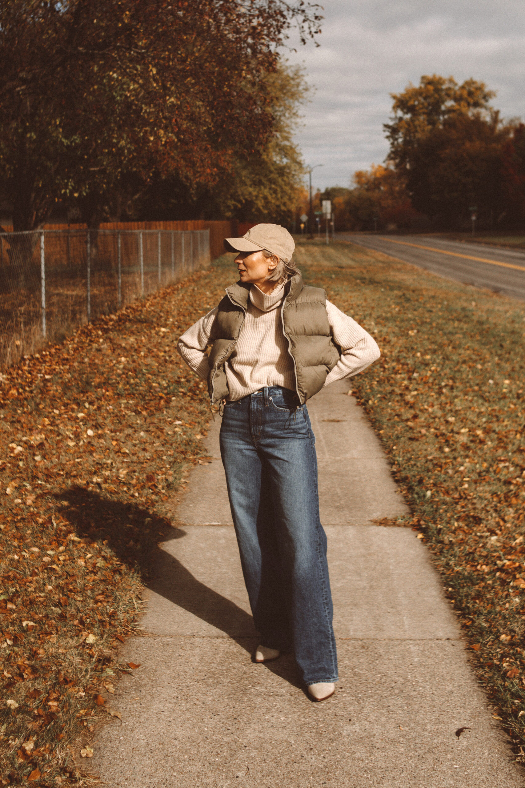 Karin Emily wears a fall mom outfit with a cropped cashmere turtleneck sweater, cropped puffer vest, wide leg jeans, and suede cowboy boots