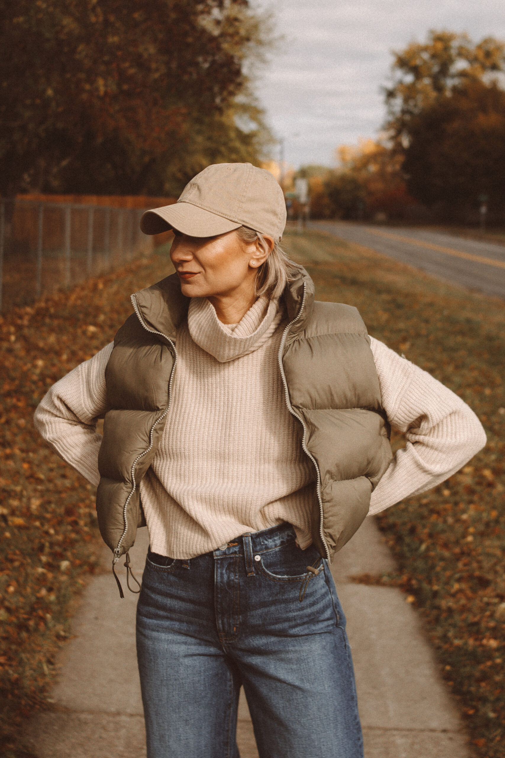 Karin Emily wears a fall mom outfit with a cropped cashmere turtleneck sweater, cropped puffer vest, wide leg jeans, and suede cowboy boots