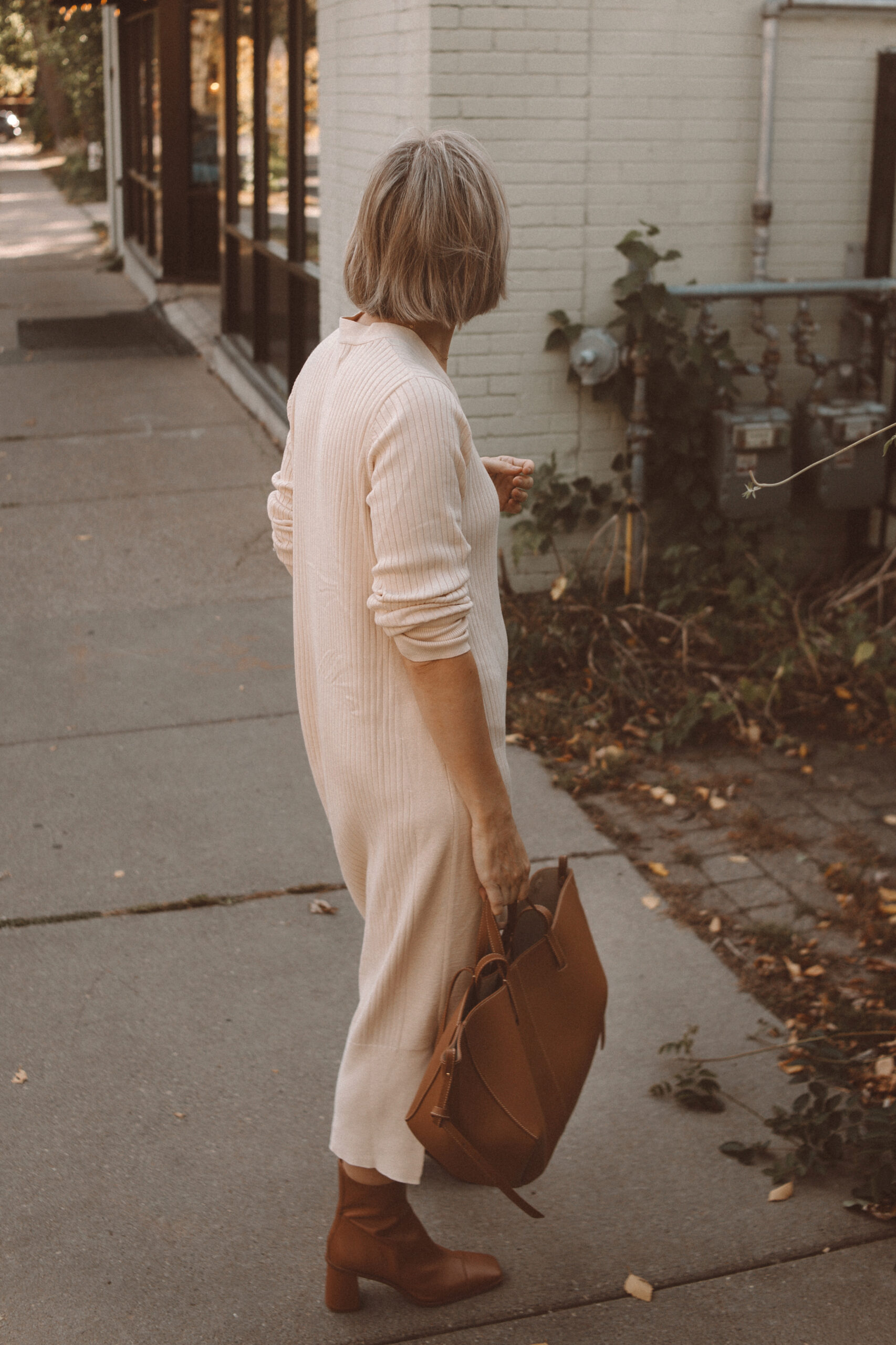Karin Emily wears a soft sweater dress with Mguire heeled sock boots and a brown Polene Bag