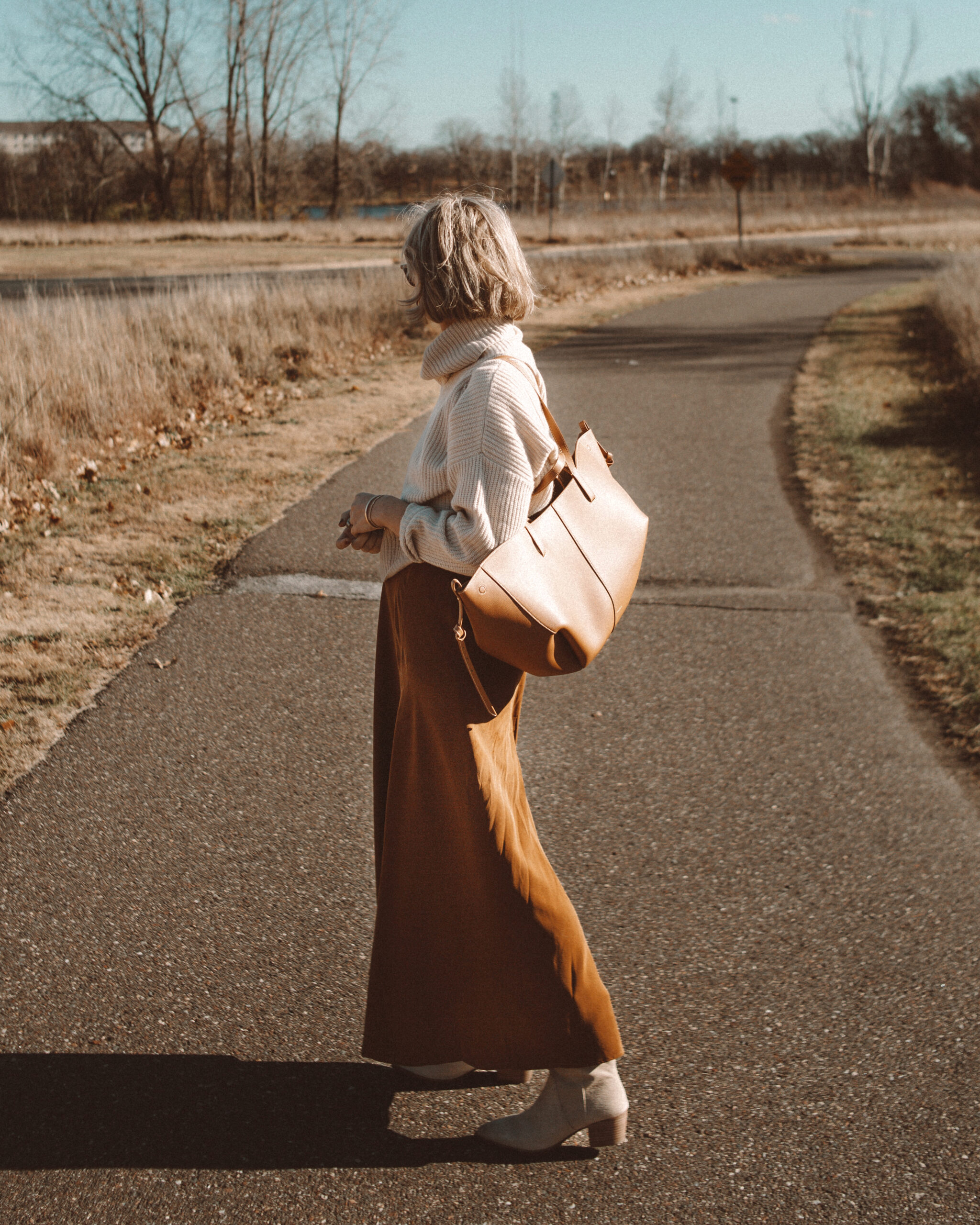 Karin Emily wears a cropped turtleneck sweater, silk maxi skirt, and taupe western boots