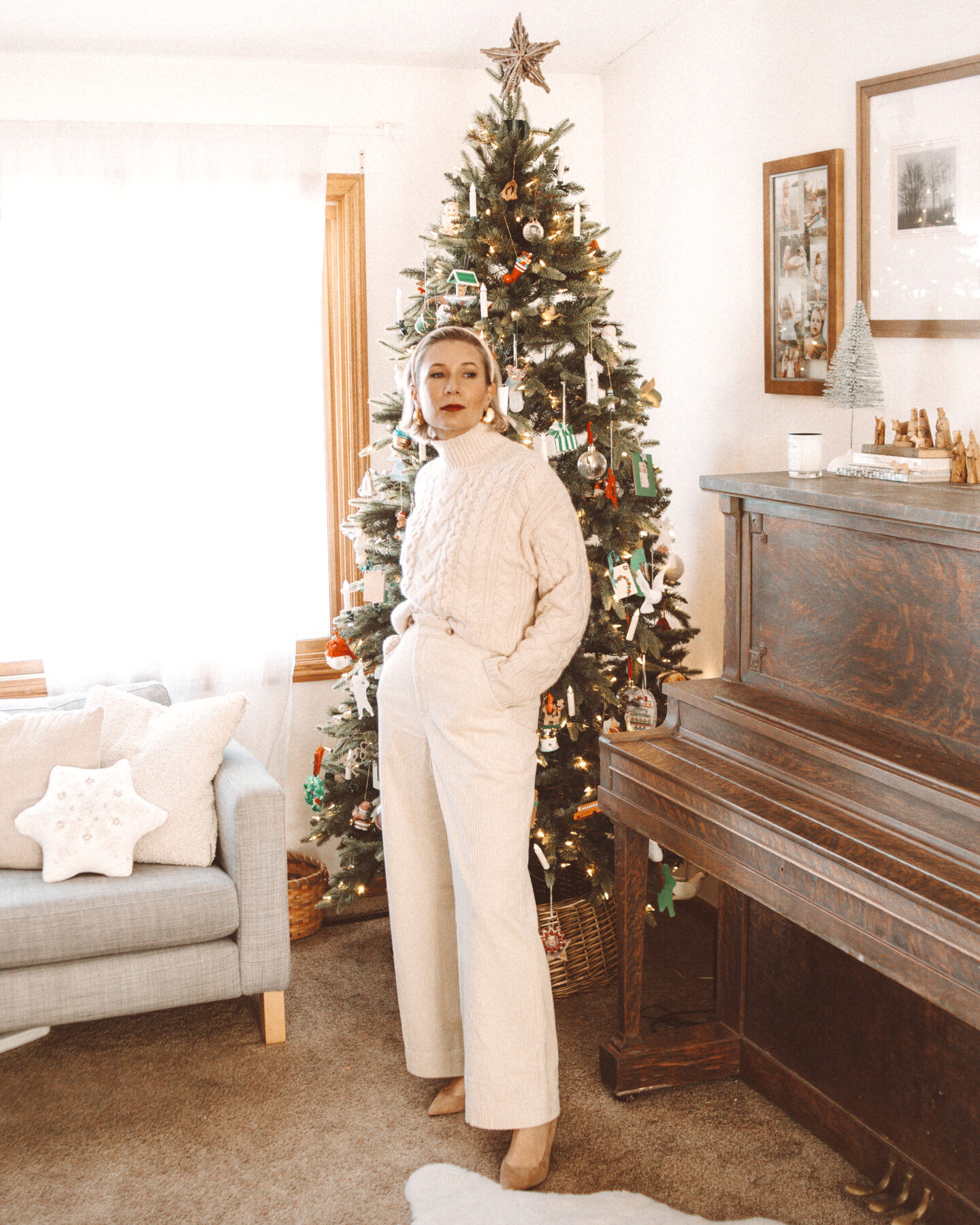Karin Emily wears a holiday party outfit with a cream turtleneck cropped sweater, cream corduroy wide leg pants, and nude heels in front of her Christmas tree
