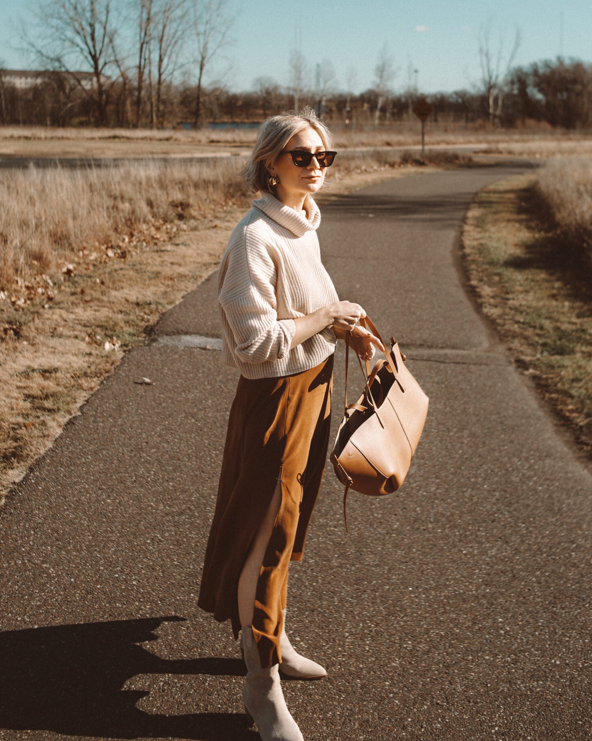 Karin Emily wears a cropped turtleneck sweater, silk maxi skirt, and taupe western boots