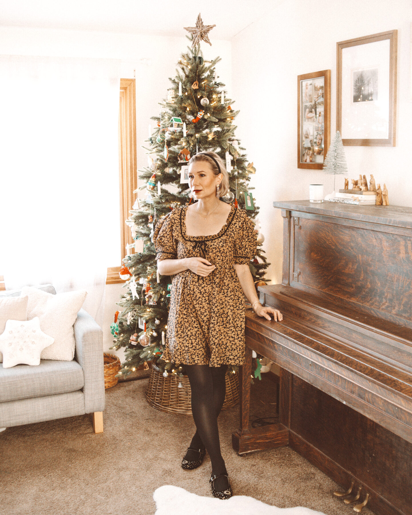 Karin Emily wears a holiday party outfit with a mini dress from Doen, black tights, and embroidered mary Jane flats in front of her Christmas tree