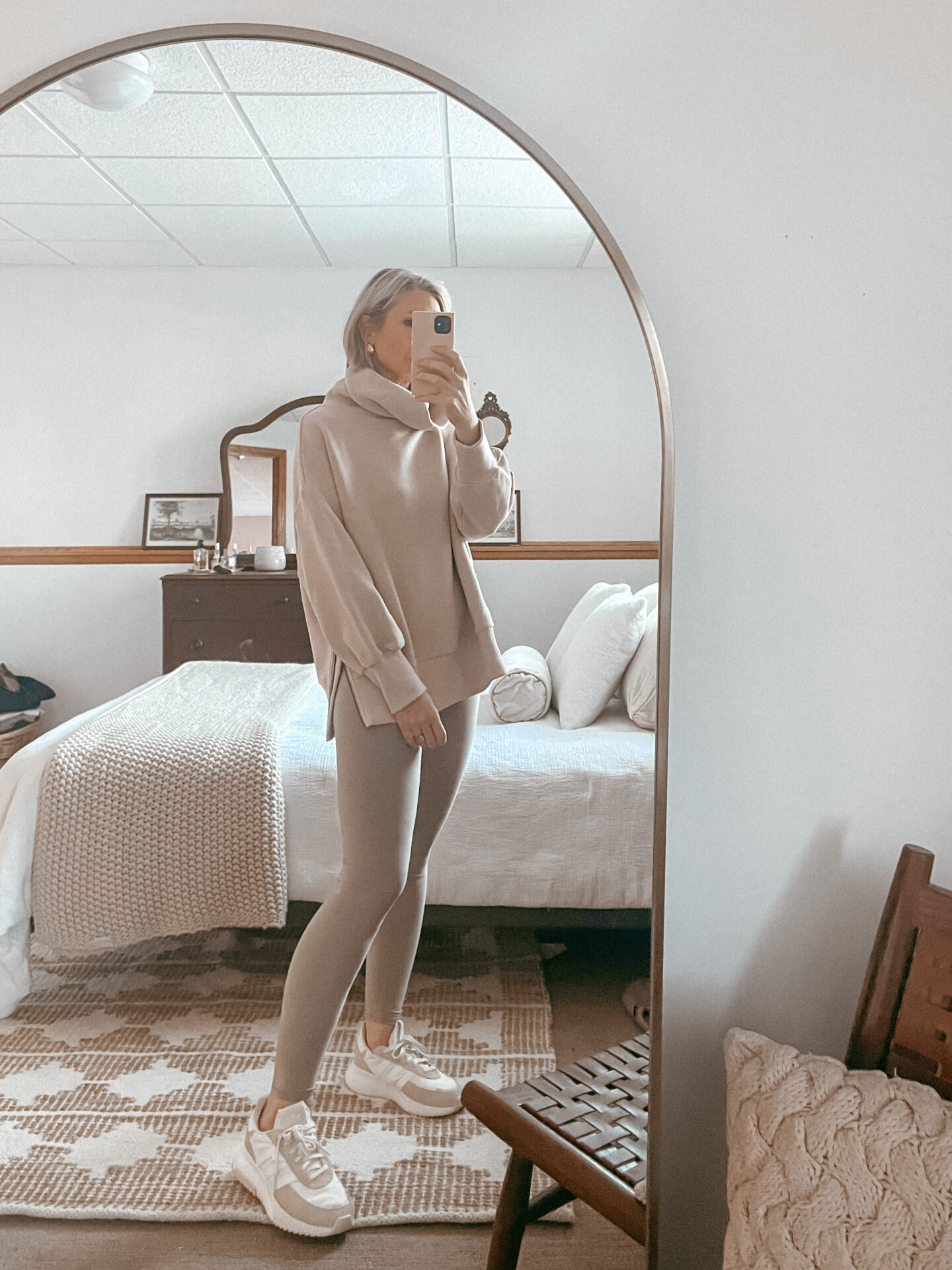 Karin Emily wears an oatmeal colored sweatshirt from Varley and oatmeal colored leggings from Alo yoga with neutral colored Adidas sneakers