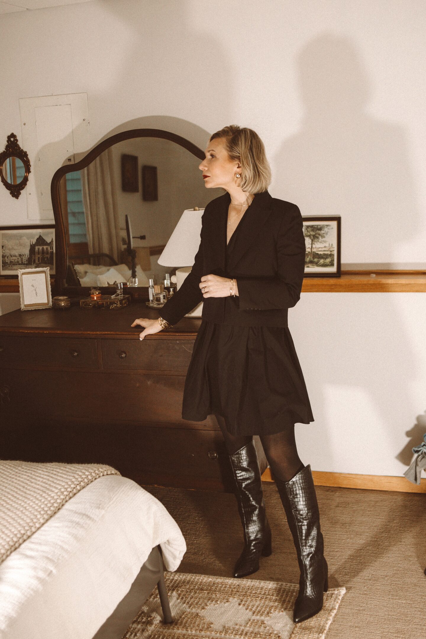 Karin Emily wears a cropped blazer with a black mini dress and black knee high Maryana boots from Schutz