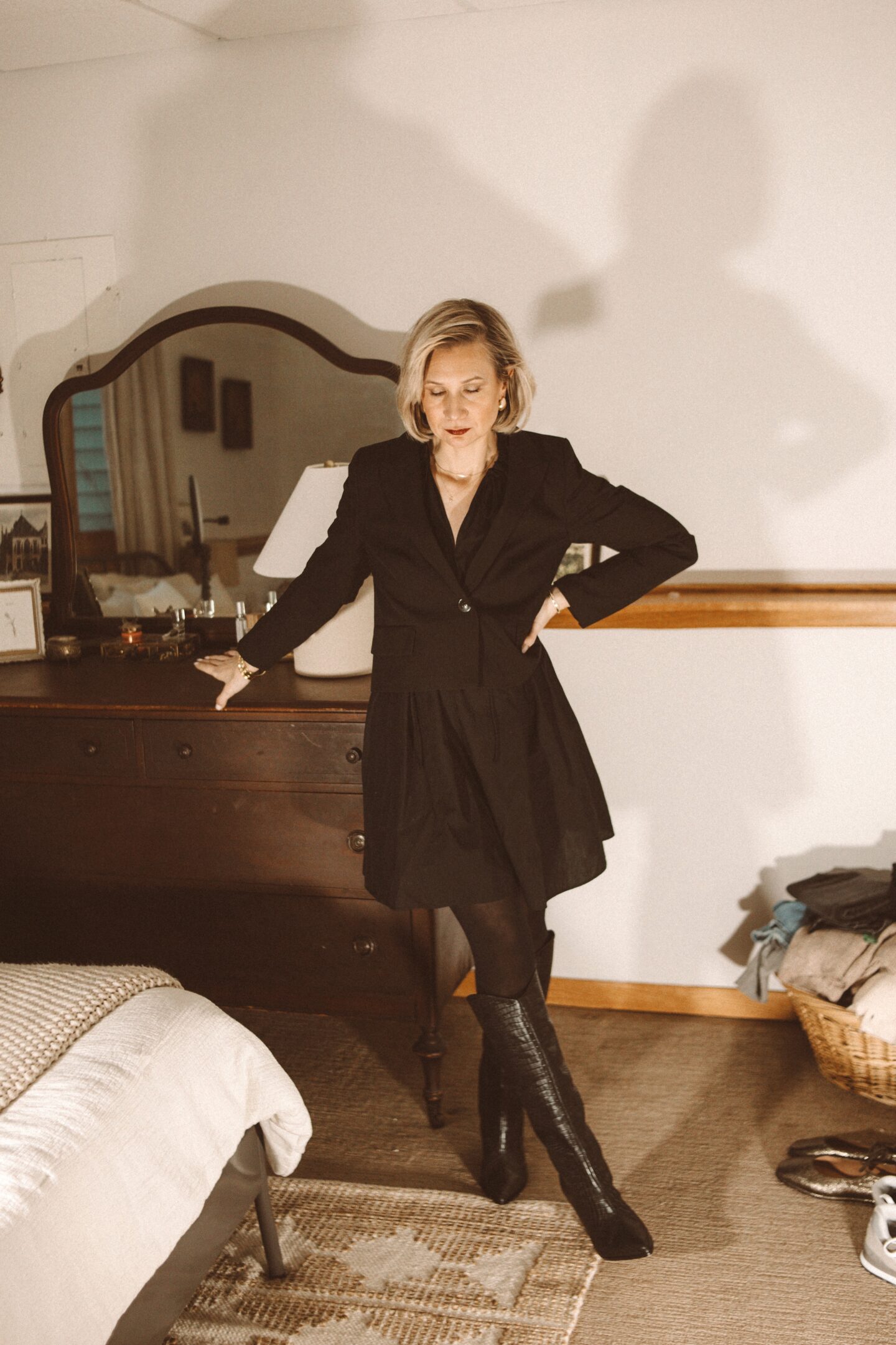 Karin Emily wears a cropped blazer with a black mini dress and black knee high Maryana boots from Schutz