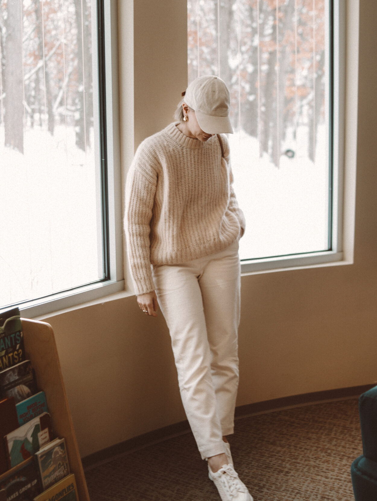 Karin Emily wears a mom uniform consisting of a cream sweater, cream pants, chunky sneakers, and a baseball hat