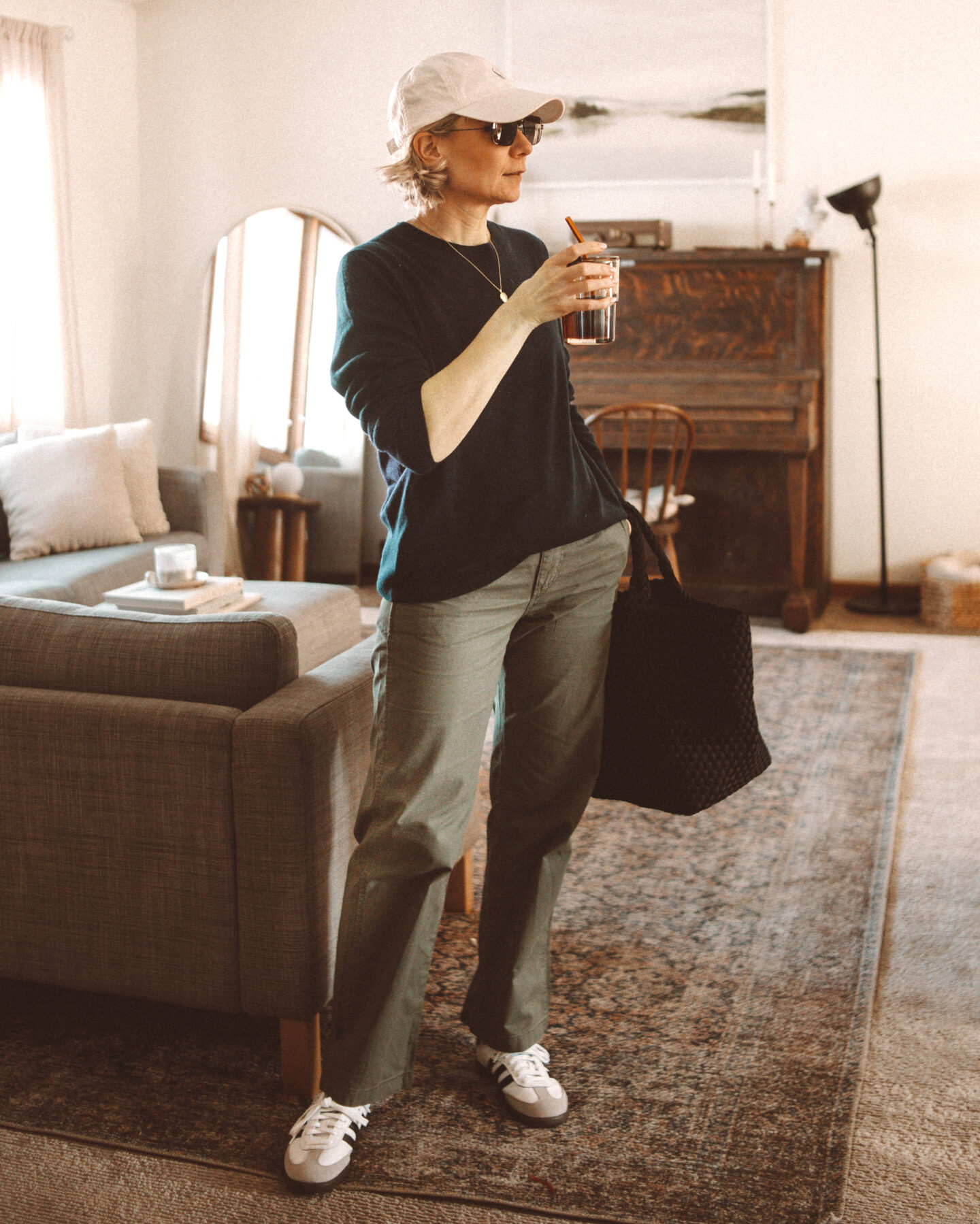 Karin Emily wears a navy blue cashmere sweater and green khaki sailor trousers from J. Crew with a pair of adidas samba sneakers and a naghedi st. Barths bag
