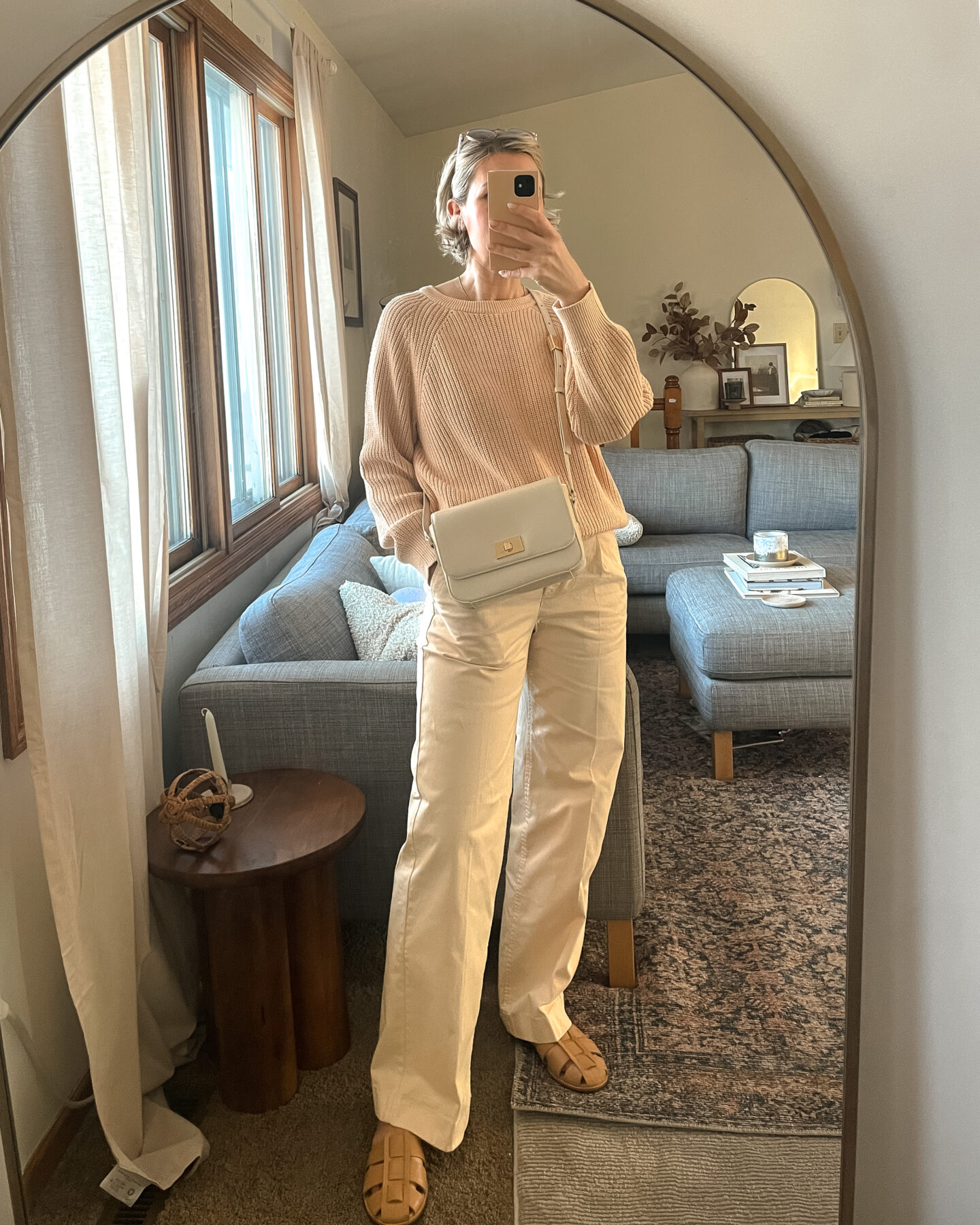 Karin Emily wears a cotton fisherman sweater and a pair of cream pleated trousers from J. Crew with a pair of sera fisherman sandals from Freda Salvador and an Edie Italian Leather Bag