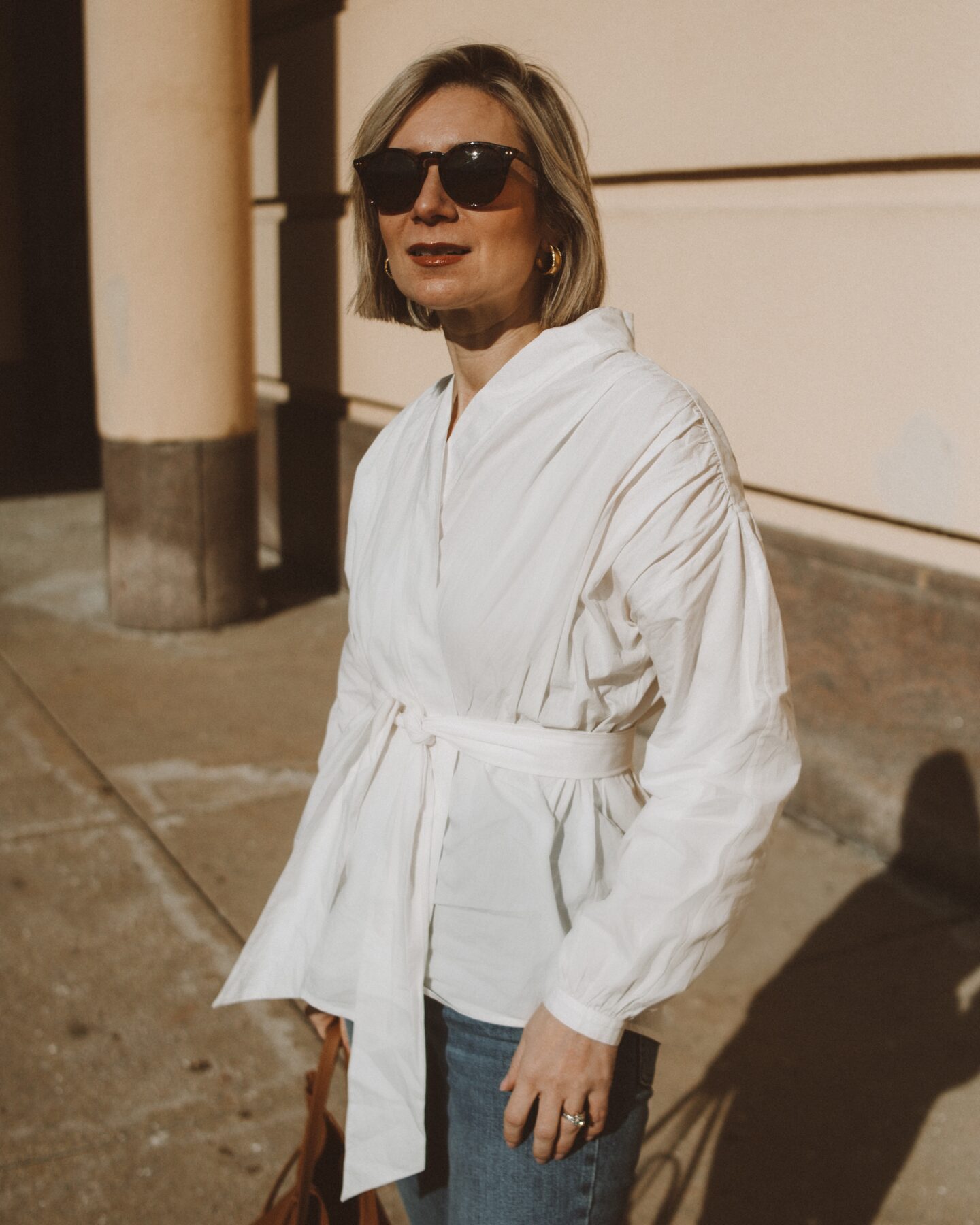 Karin Emily wears a white cotton wrap blouse with a pair of classic tortoiseshell sunglasses