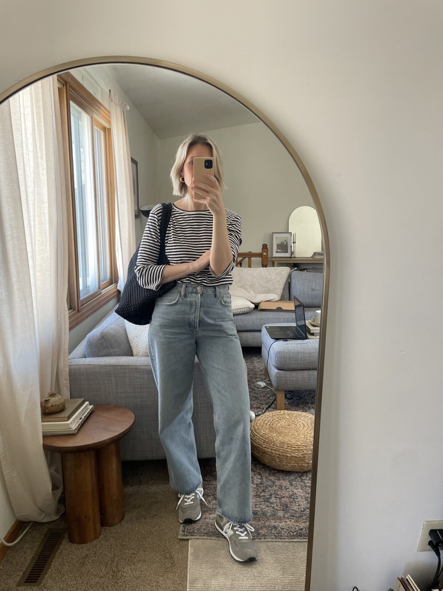 Karin Emily stands in front of a mirror wearing a striped shirt, gray new balance sneakers and baggy jeans 