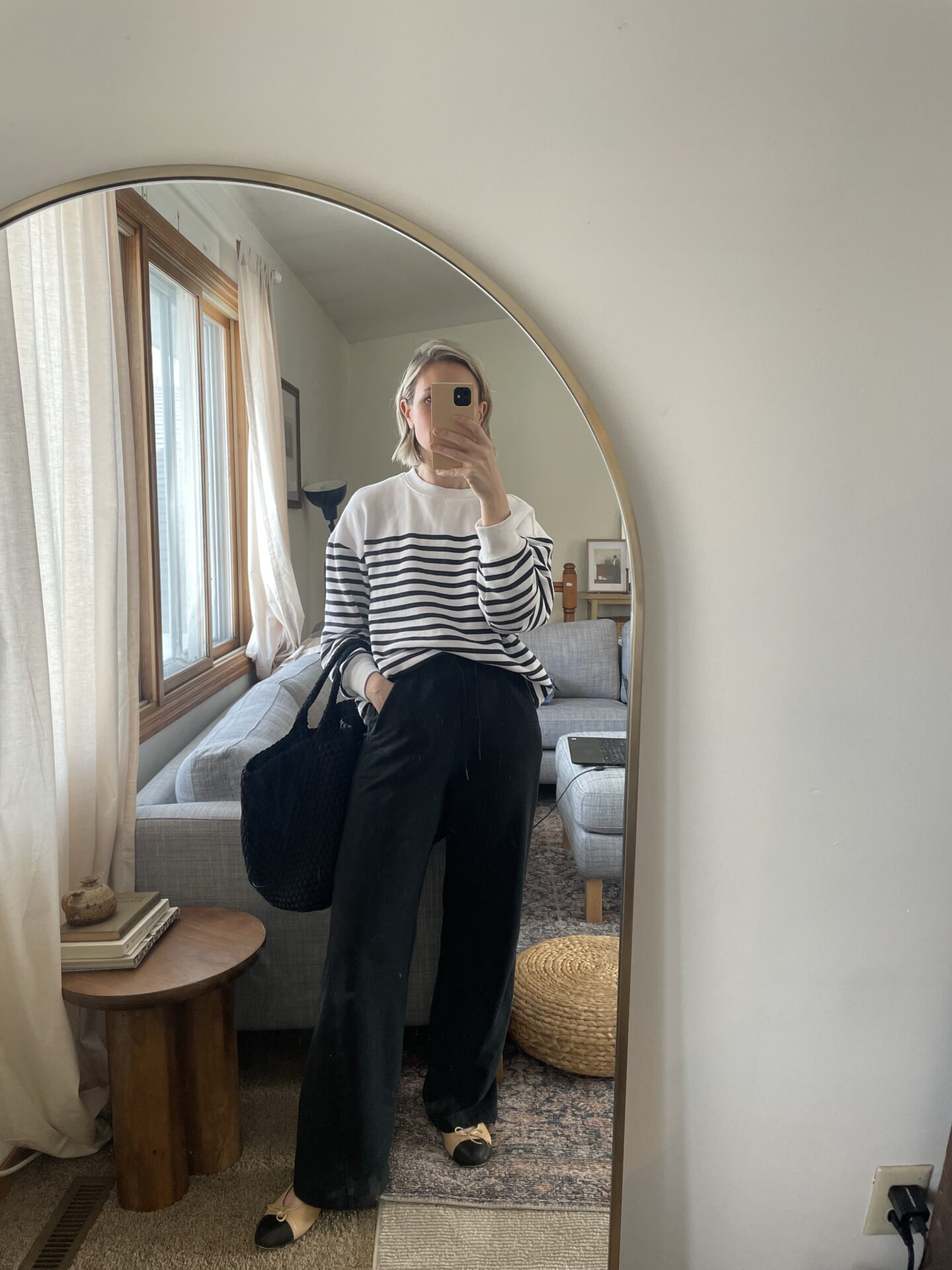 girl stands in front of a mirror with a striped sweatshirt, black wide leg sweatpants and two tone flats on