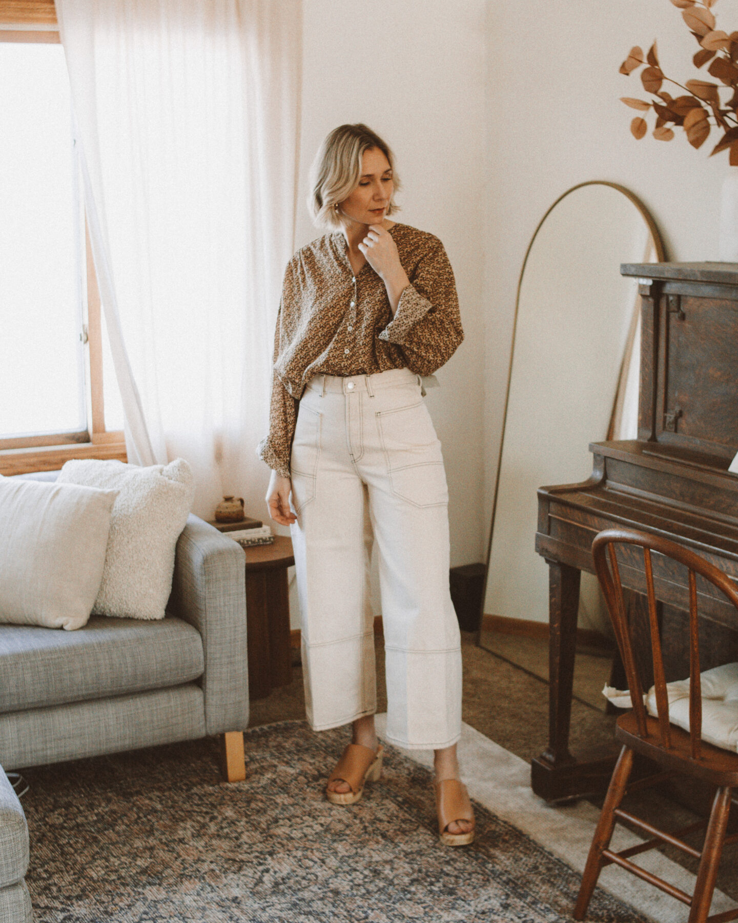 Karin Emily wears a pair of cargo jeans from Everlane and a floral blouse while standing in her living room