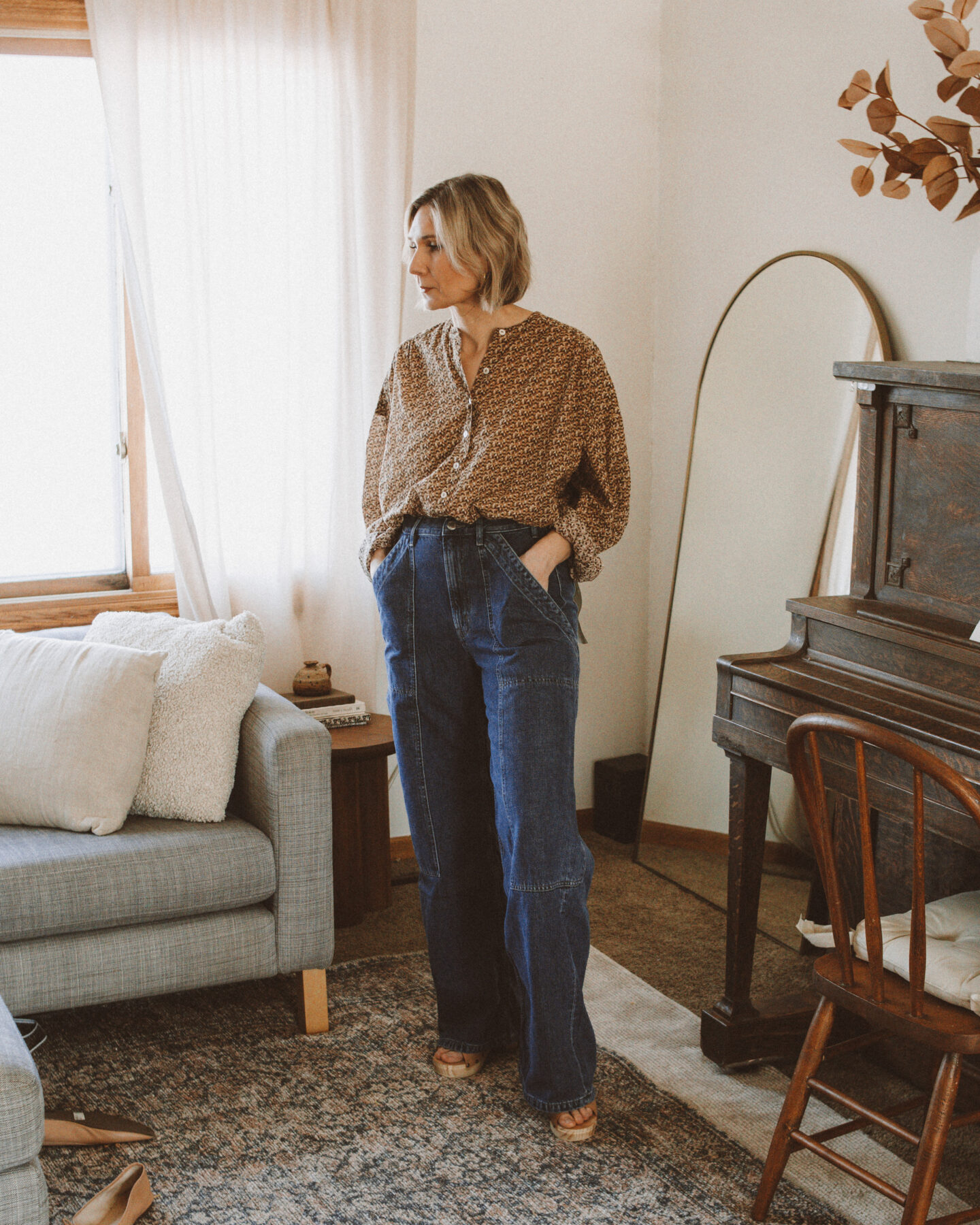 Karin Emily wears a pair of cargo jeans from Everlane and a floral blouse while standing in her living room