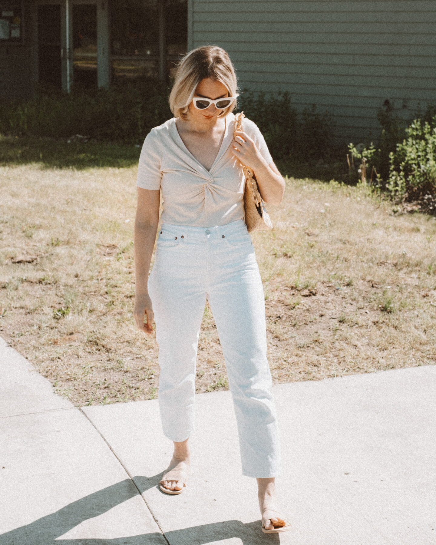 Karin Emily holds a basket bag embroidered with daisies from Sezane while wearing a knitted t-shirt and standing in front of a navy blue building 