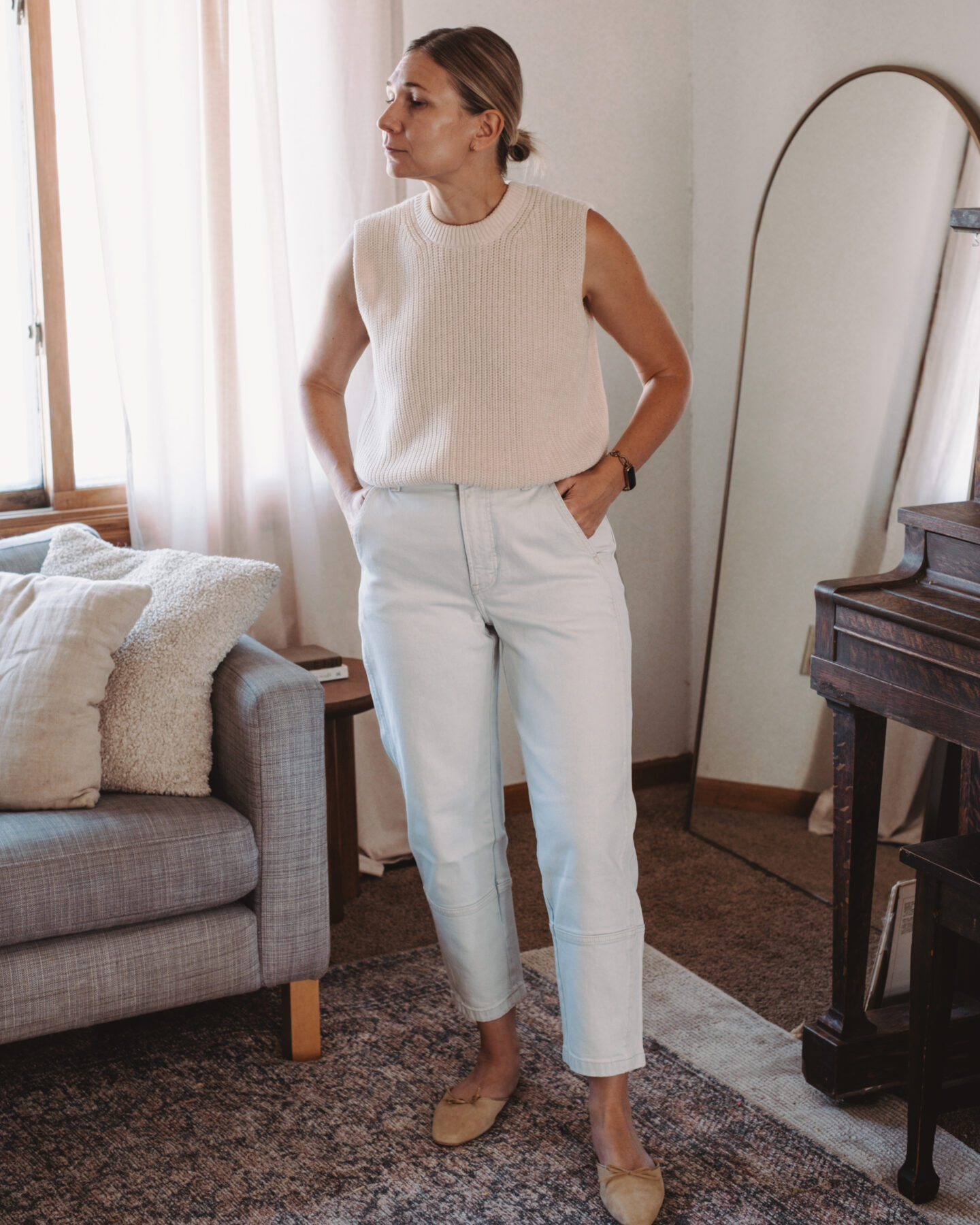 Karin Emily stands in her living room wearing a pair of barrel leg jeans and a sweater tank