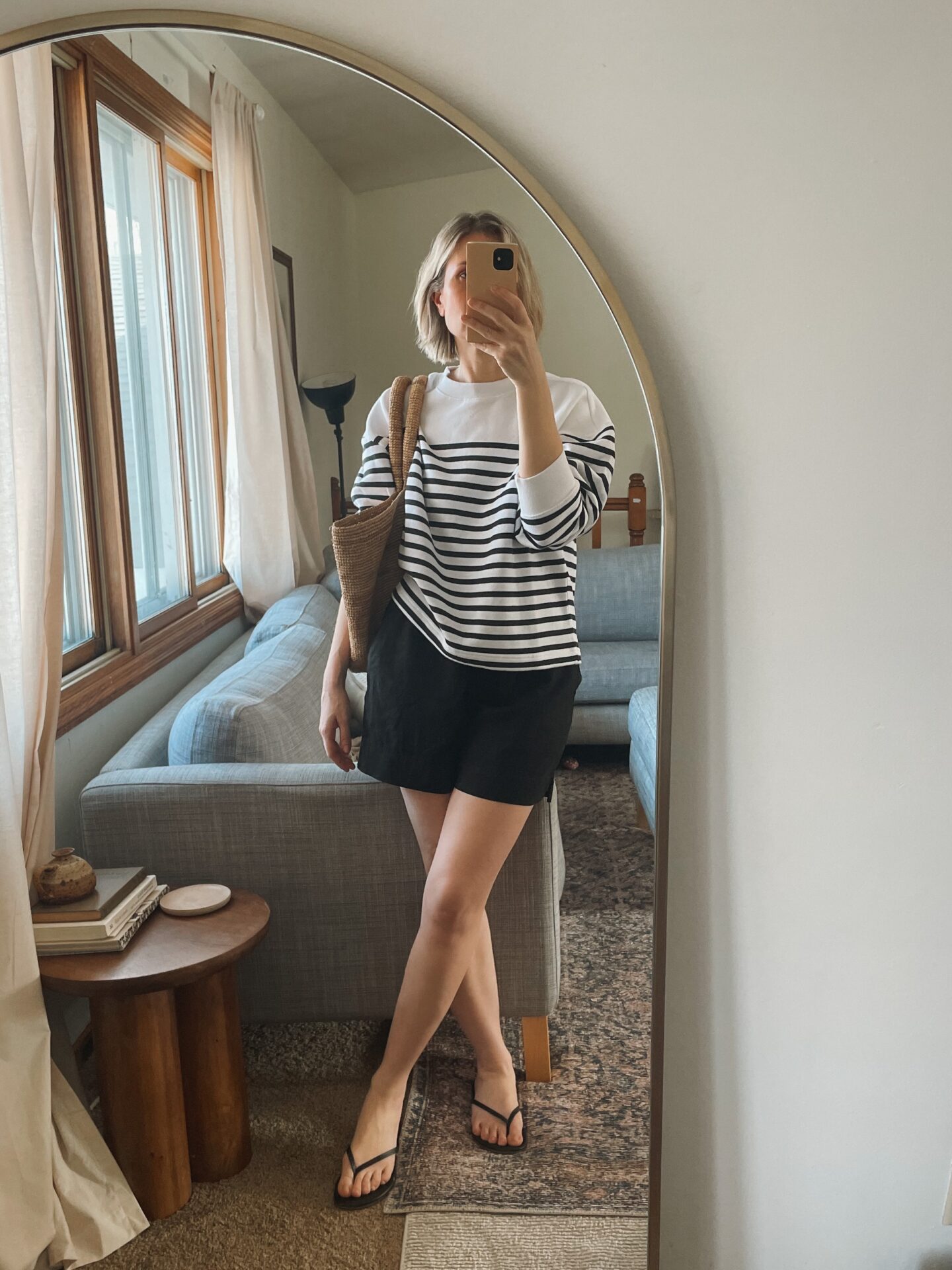 Karin Emily takes a mirror selfie in her living room and wears a striped sweatshirt with black linen shorts