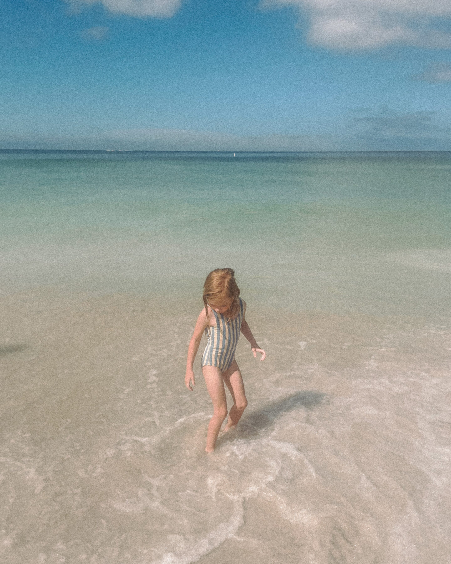 A little girl twirls in the ocean water on the beach