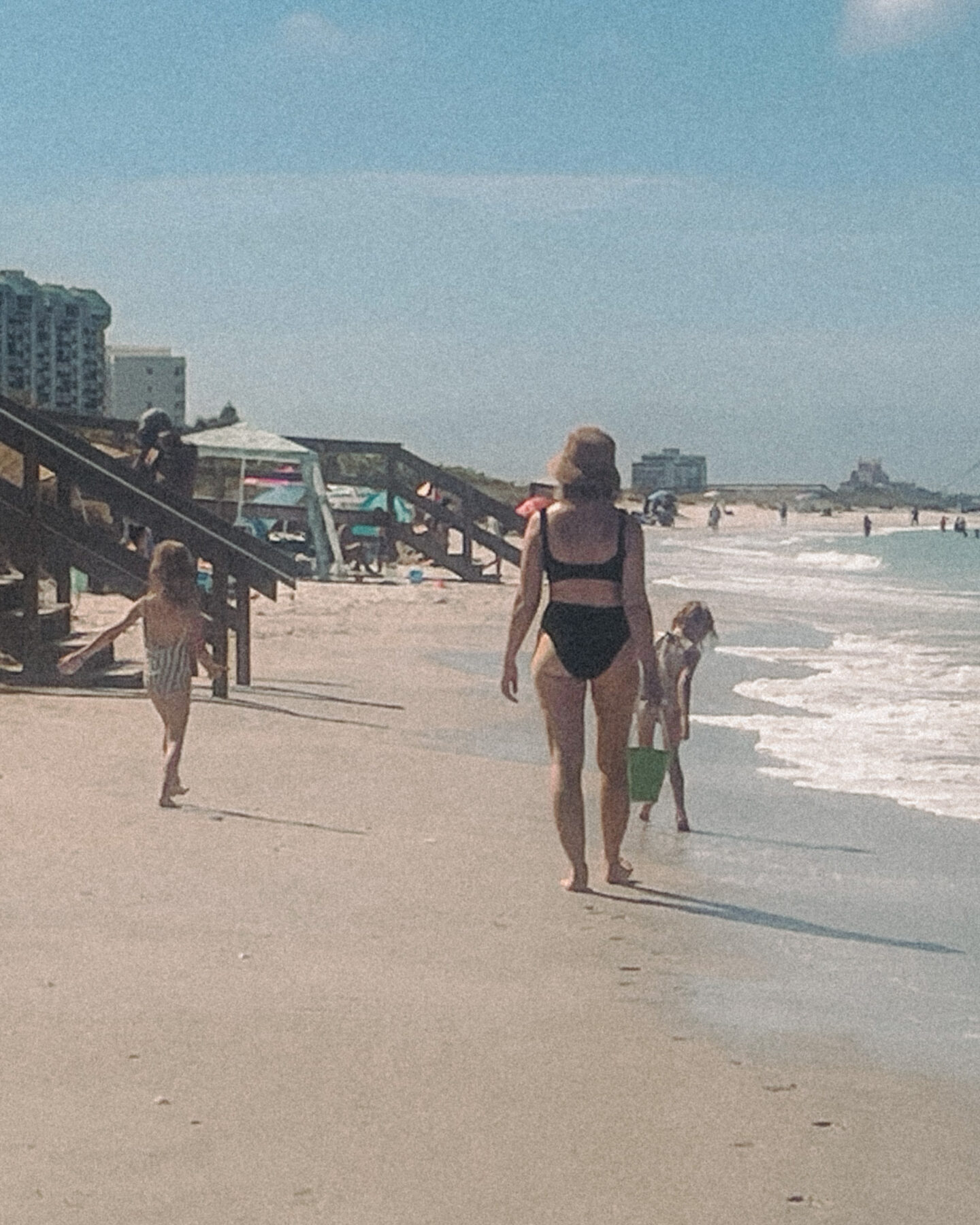 Karin Emily wearing a Hunza G bikini walks on the beach with her twin daughters