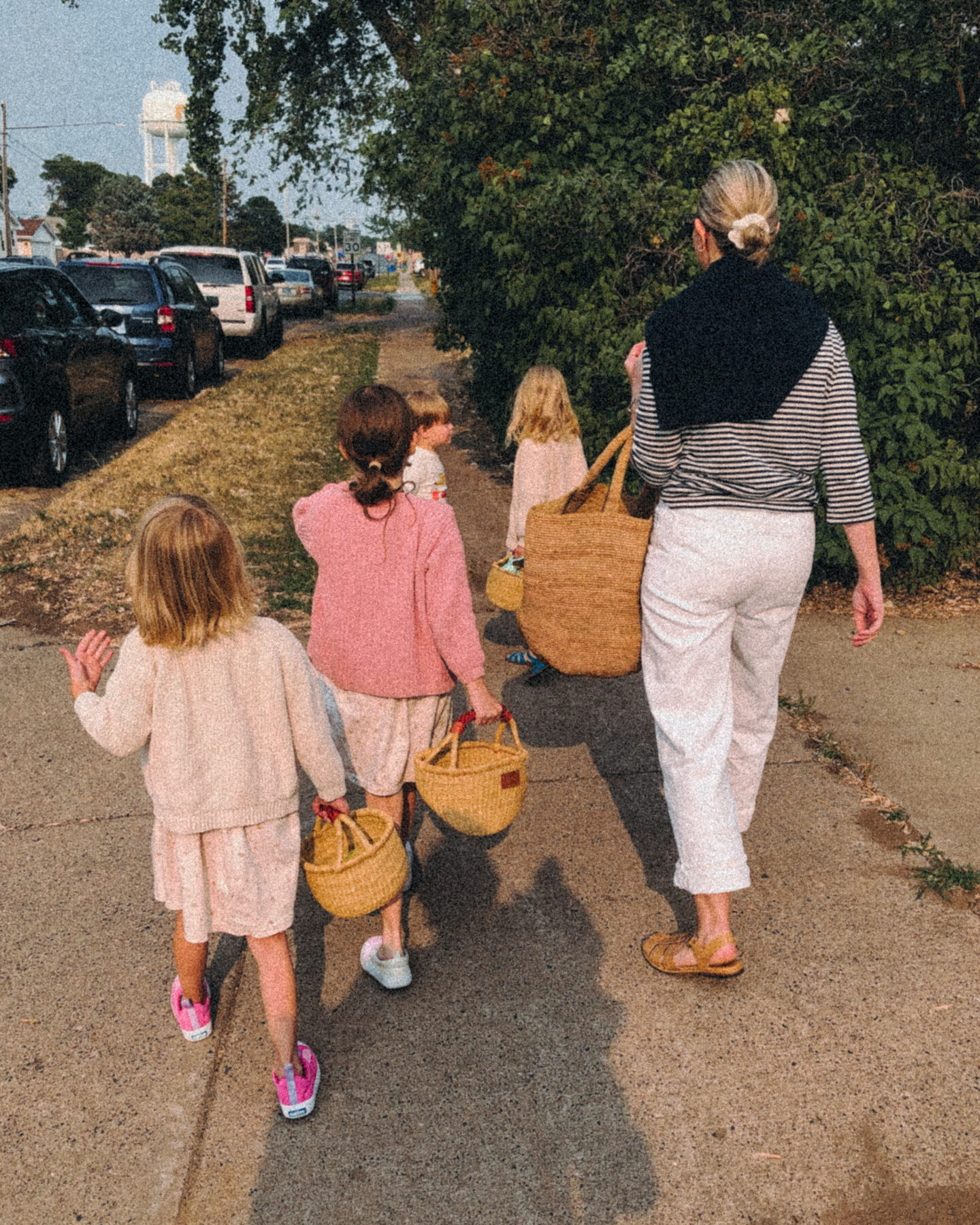 Karin Emily walks with her kids on a sidewalk and wears a black and white striped long sleeve tee white baggy jeans from agolde, nude fisherman sandals, a basket bag, and a navy cashmere sweater over her shoulders