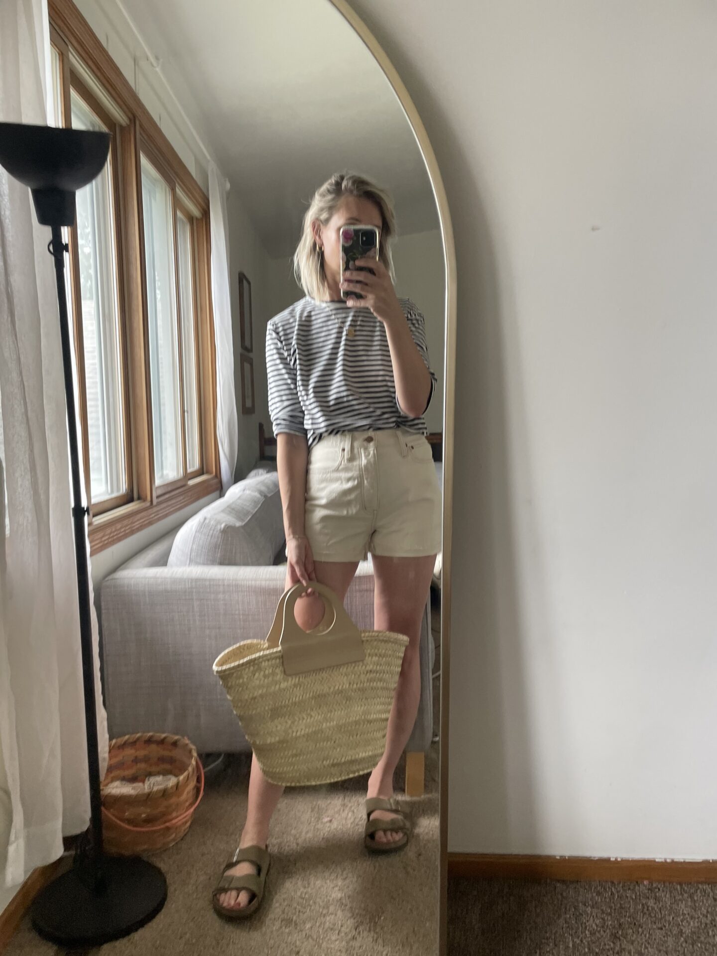 Karin Emily takes a mirror selfie wearing a striped long sleeve tee and cream colored denim shorts with a Hereu basket bag