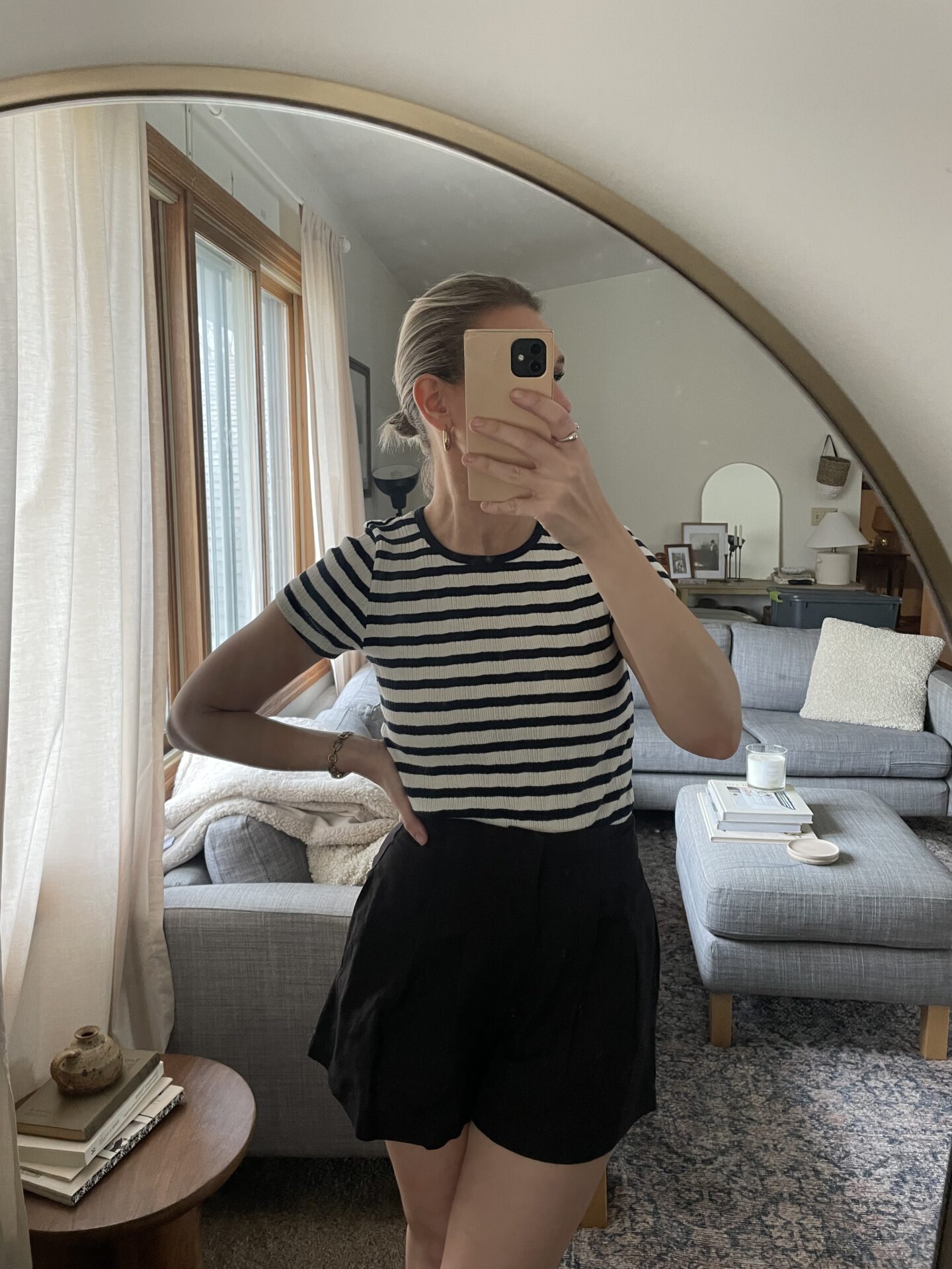 Karin Emily takes a mirror selfie and wears a short sleeve black and white tee from Doen and a pair of black cotton pleated shorts