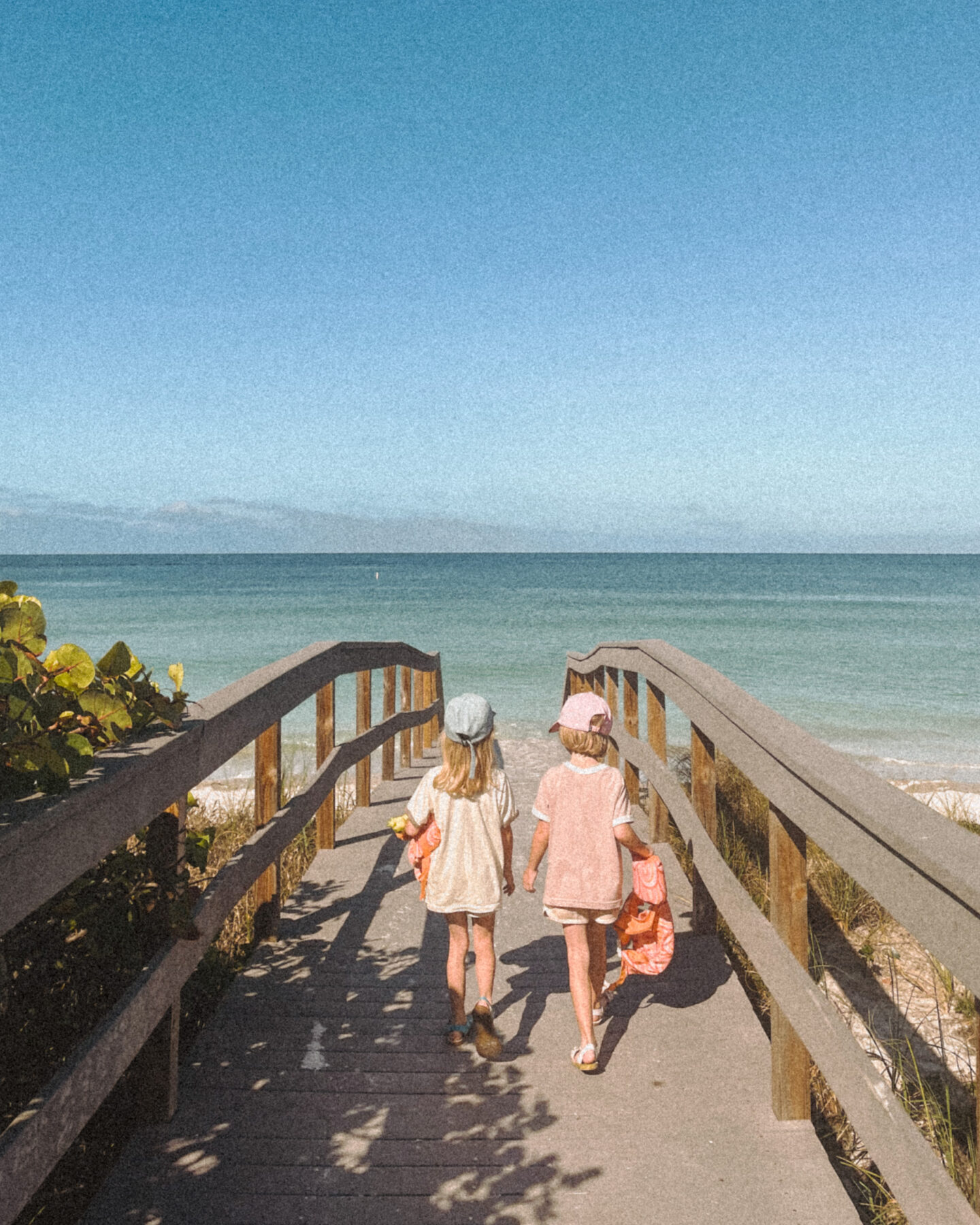 Twin girls walk along a boardwalk on the way to the beach