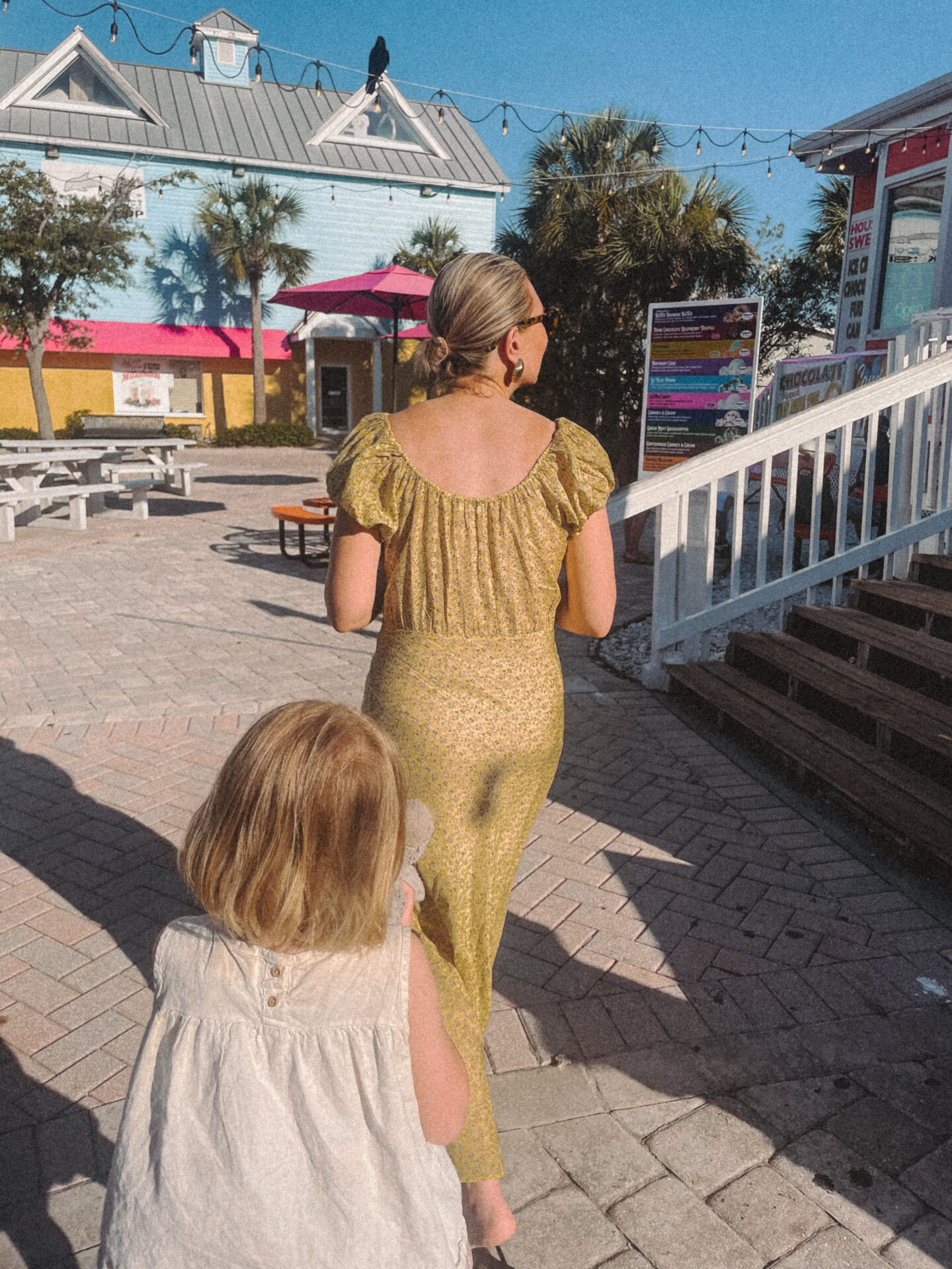 Karin Emily wearing a long yellow dress from Doen walks into a beach candy shop with her twin daughters