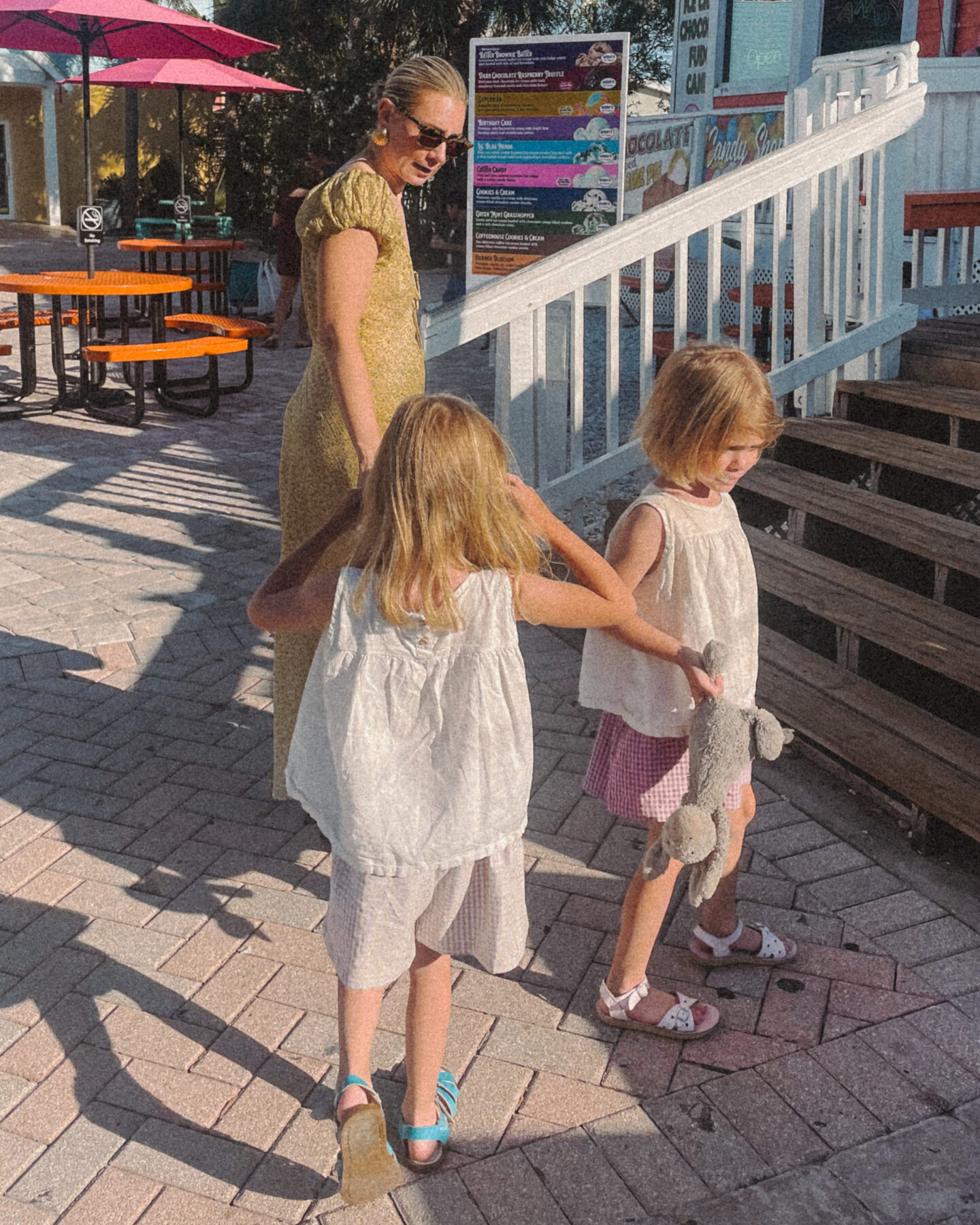 Karin Emily wearing a long yellow dress from Doen walks into a beach candy shop with her twin daughters