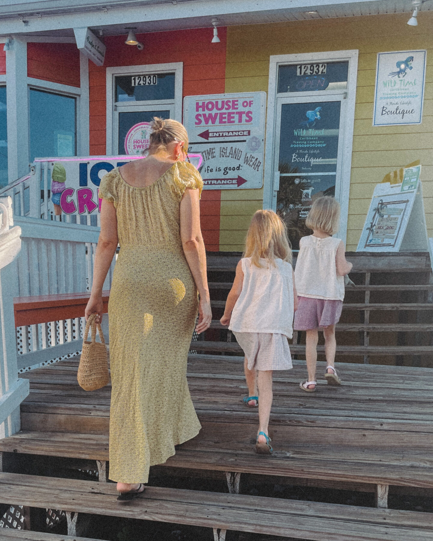 Karin Emily wearing a long yellow dress from Doen walks into a beach candy shop with her twin daughters