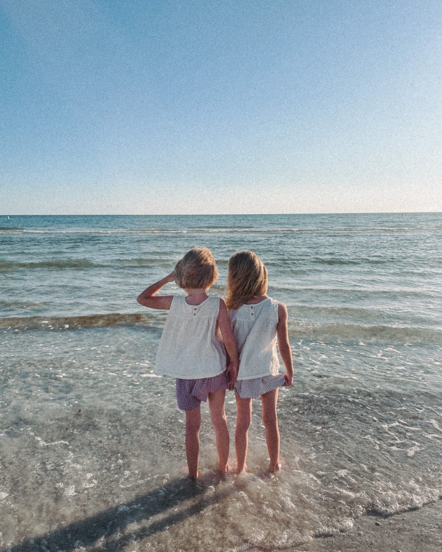 Twin girls stand and look out at the ocean