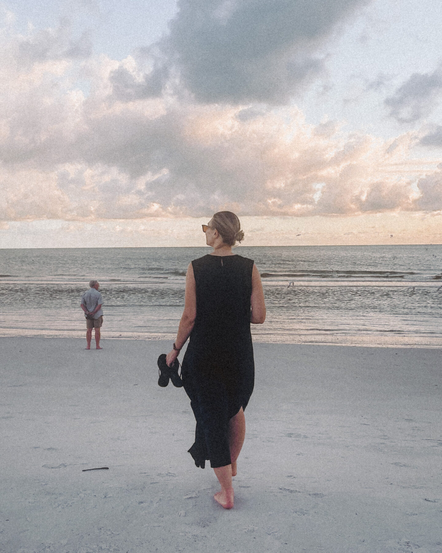 Karin Emily walks down to the water on the beach wearing a black linen dress from J. Crew