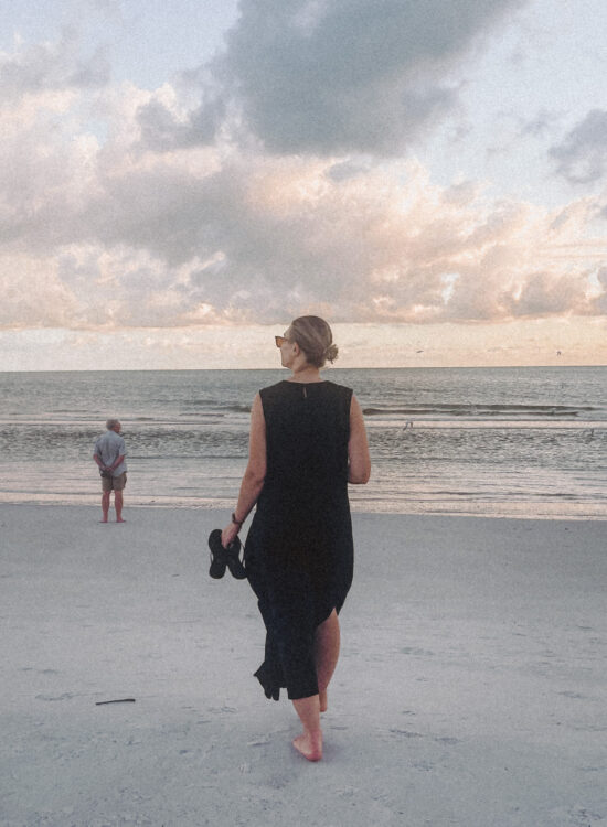 Karin Emily walks down to the water on the beach wearing a black linen dress from J. Crew