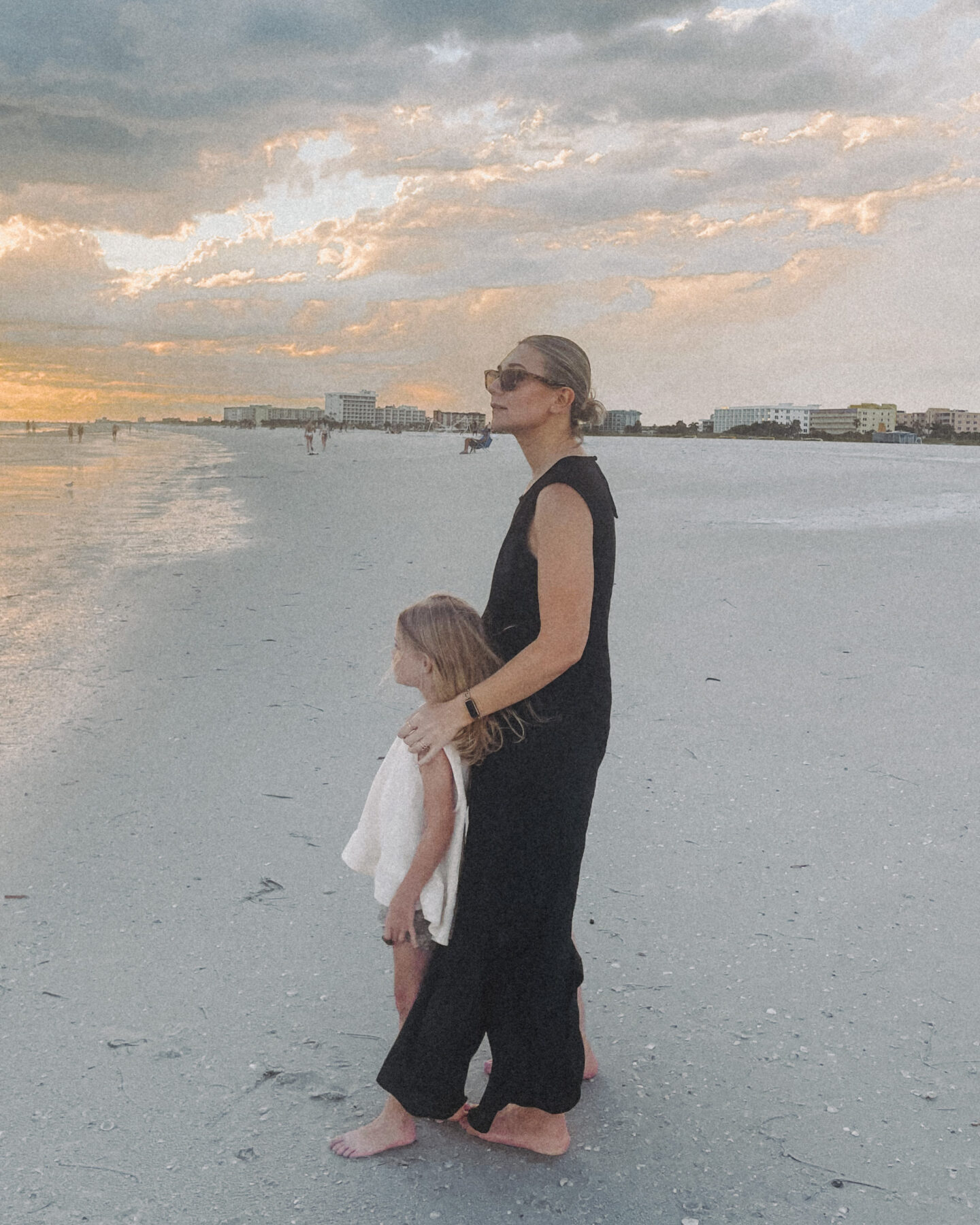 Karin Emily wearing a black line dress from J. Crew twirls her daughter while on the beach