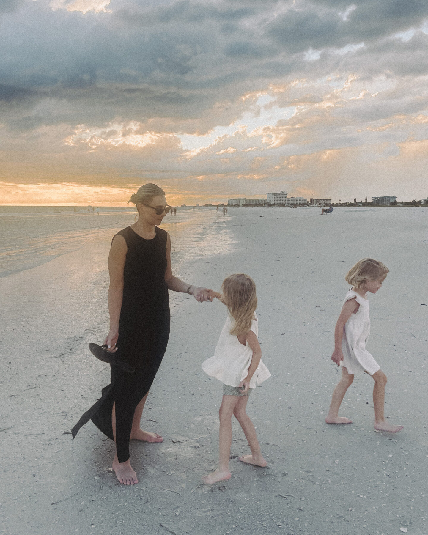 Karin Emily wearing a black line dress from J. Crew twirls her daughter while on the beach