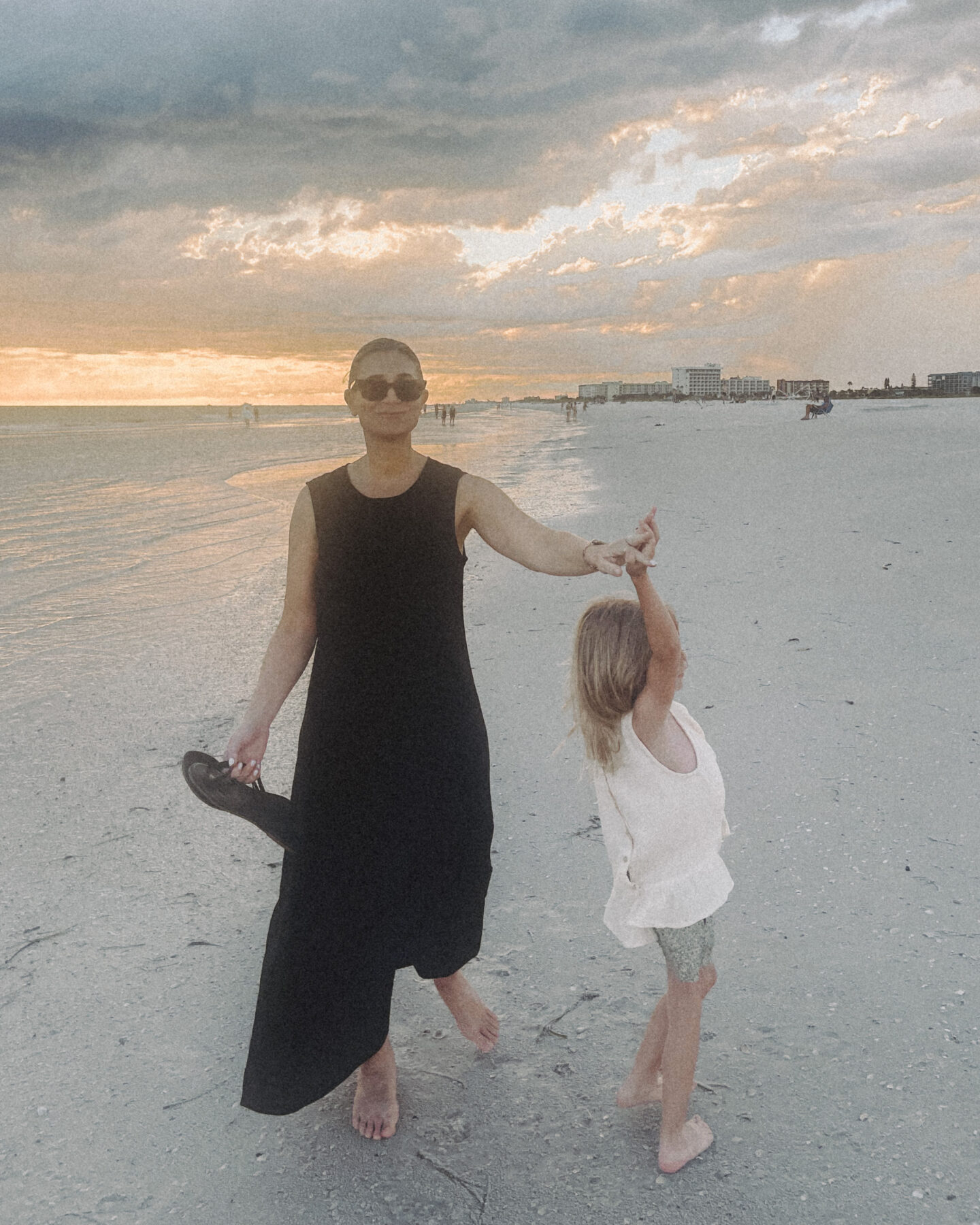 Karin Emily wearing a black line dress from J. Crew twirls her daughter while on the beach