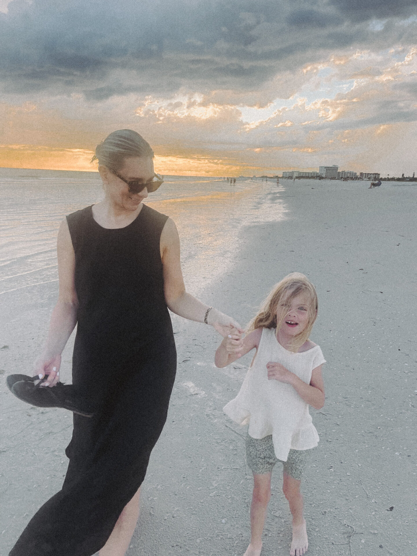 Karin Emily wearing a black line dress from J. Crew twirls her daughter while on the beach