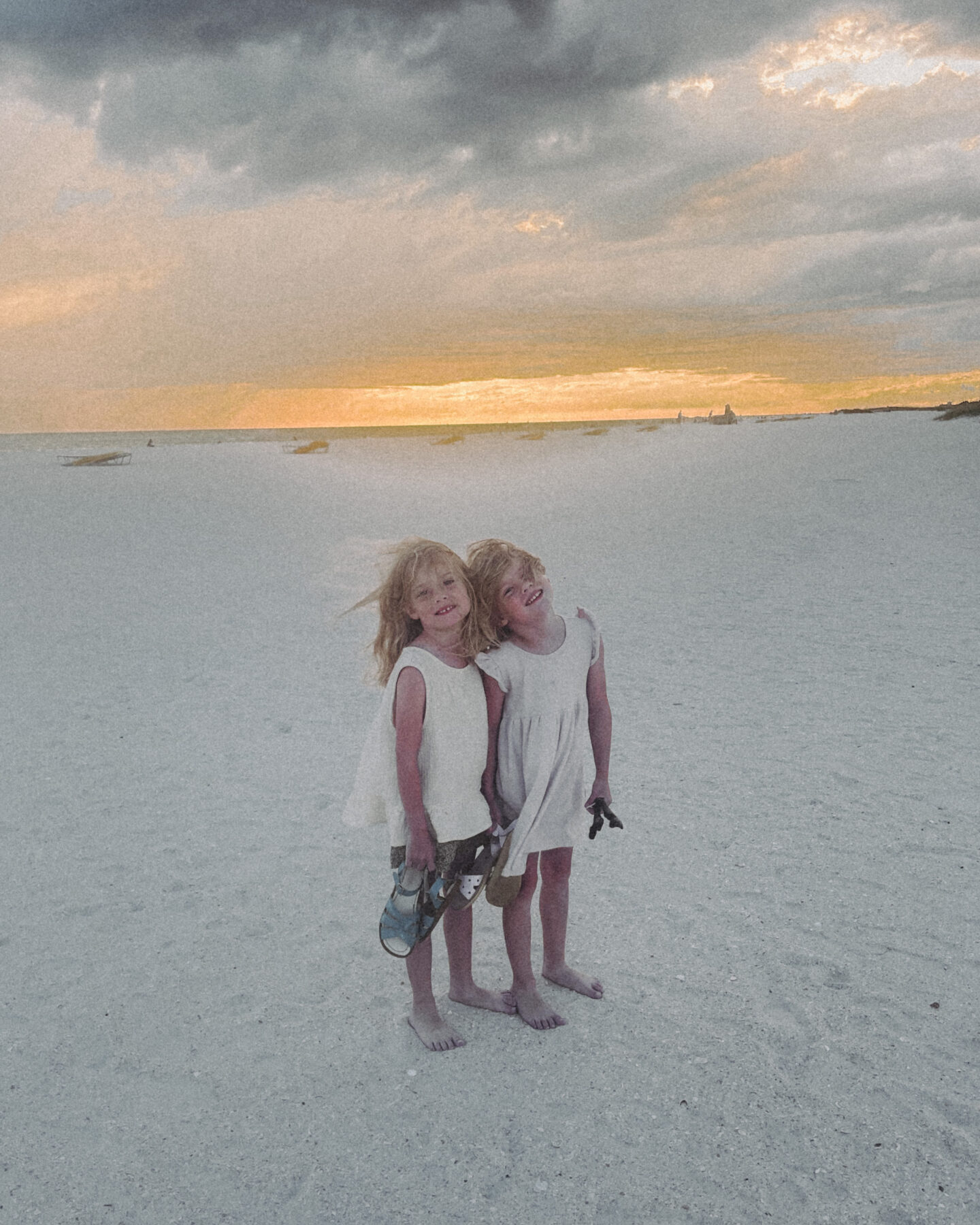 Two twin girls standing together on the beach