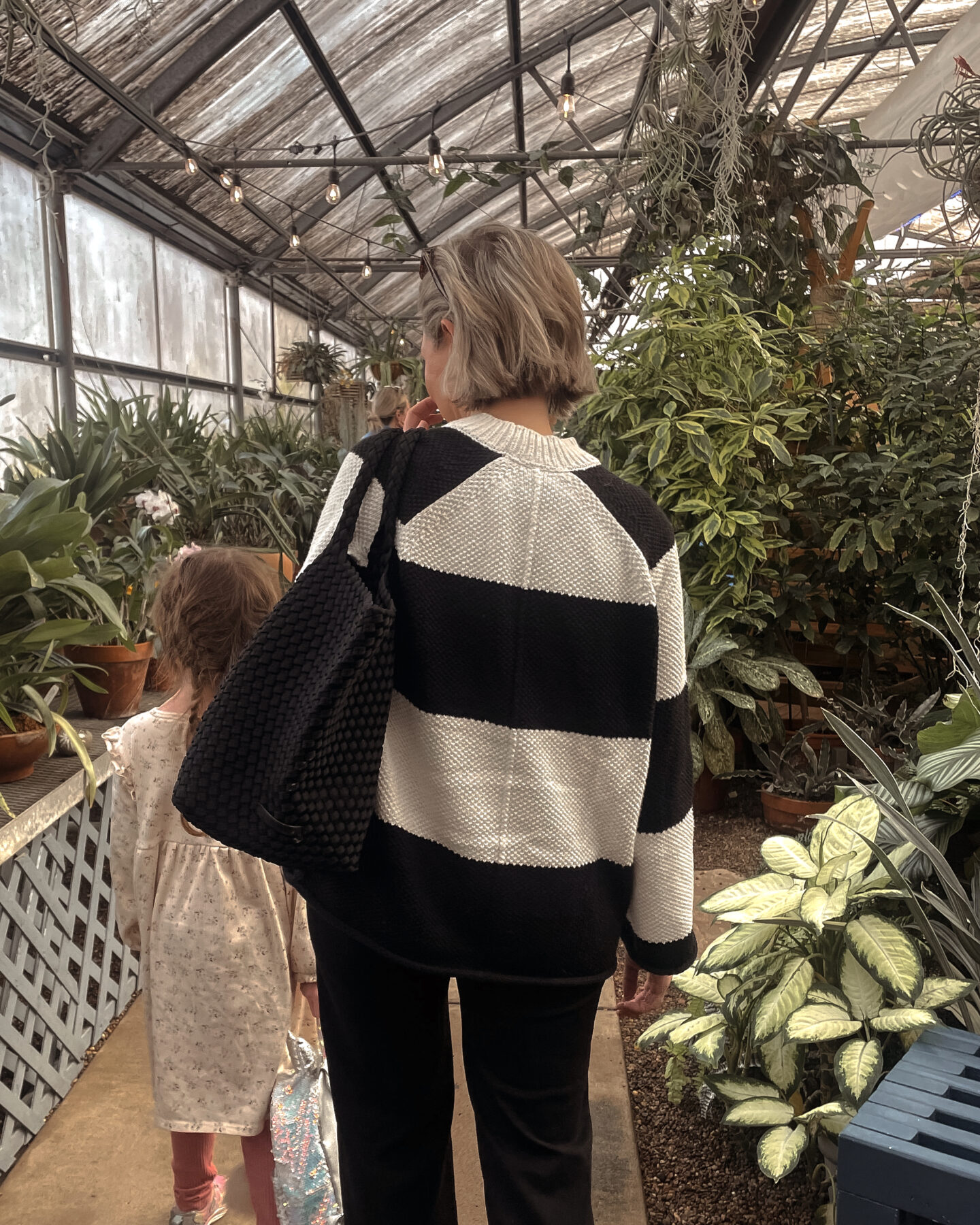 Karin Emily walks with her daughter in an arboretum and wears a striped sweater and black wide leg pants