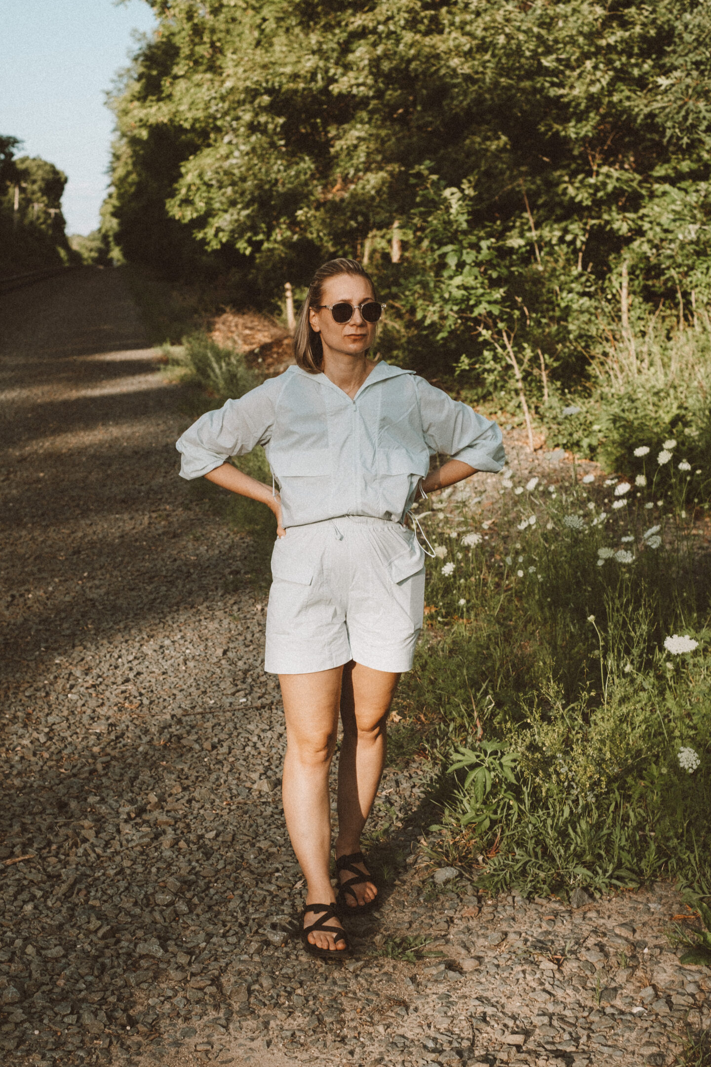 Karin Emily wears a hiking set from NEIWAI while standing in front of an outdoor wooded area dotted with wildflowers