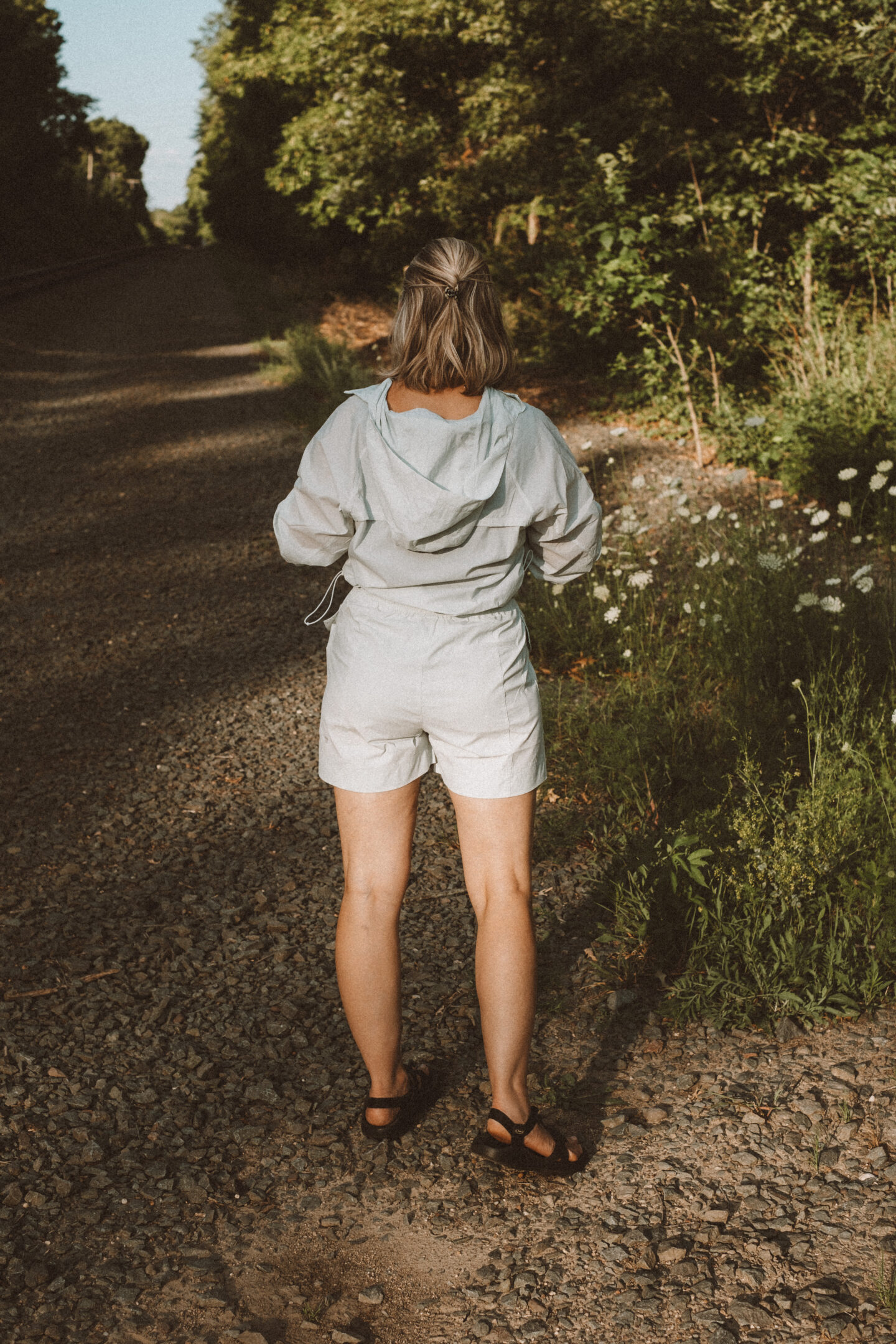 Karin Emily wears a hiking set from NEIWAI while standing in front of an outdoor wooded area dotted with wildflowers