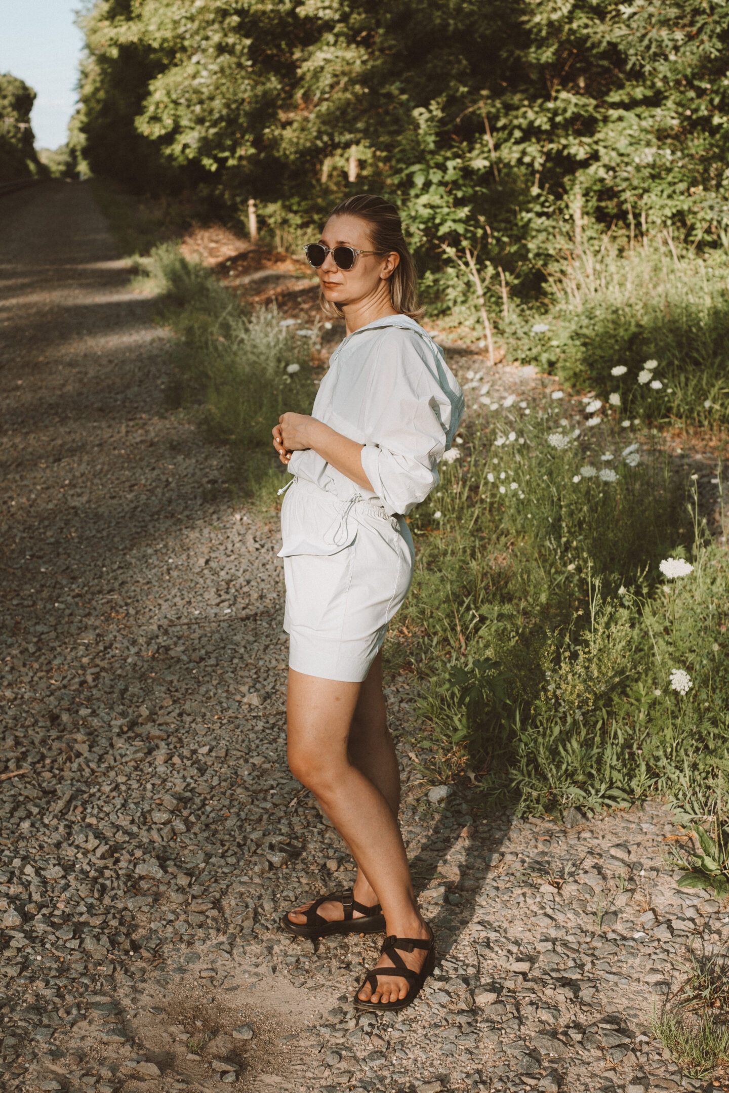 Karin Emily wears a hiking set from NEIWAI while standing in front of an outdoor wooded area dotted with wildflowers