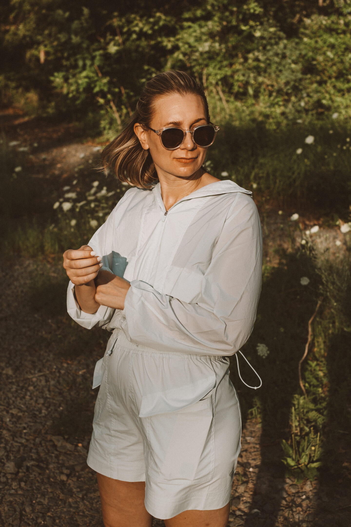 Karin Emily wears a hiking set from NEIWAI while standing in front of an outdoor wooded area dotted with wildflowers