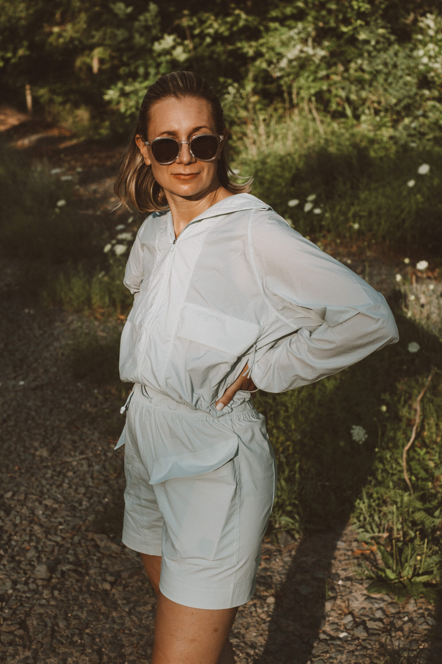 Karin Emily wears a hiking set from NEIWAI while standing in front of an outdoor wooded area dotted with wildflowers