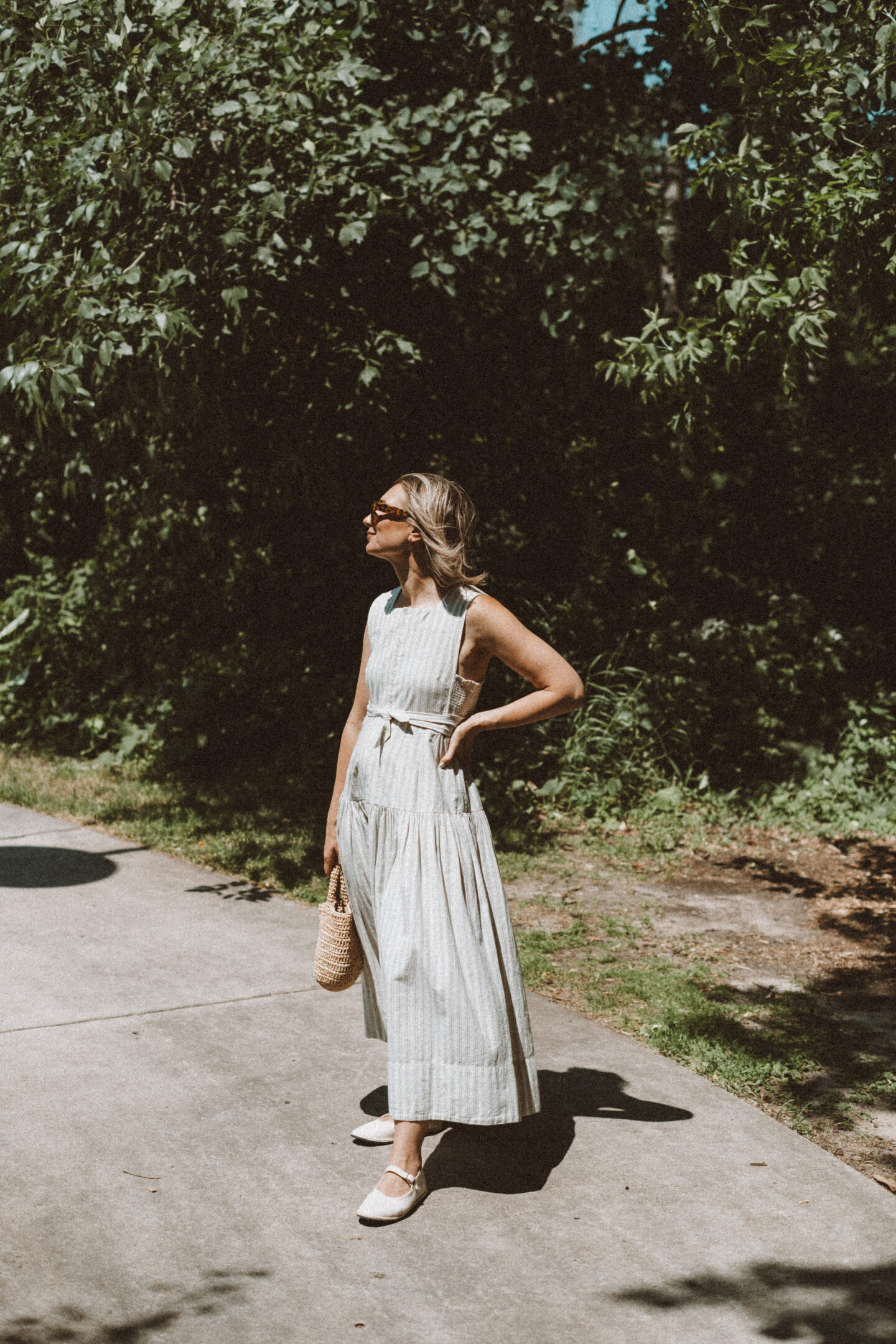 Karin Emily wears a Doen dress from her Capsule Wardrobe, a pair of White Mary Jane shoes while standing in front of the woods on a path