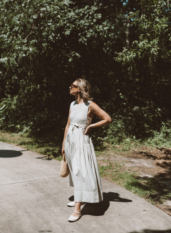 Karin Emily wears a Doen dress from her Capsule Wardrobe, a pair of White Mary Jane shoes while standing in front of the woods on a path